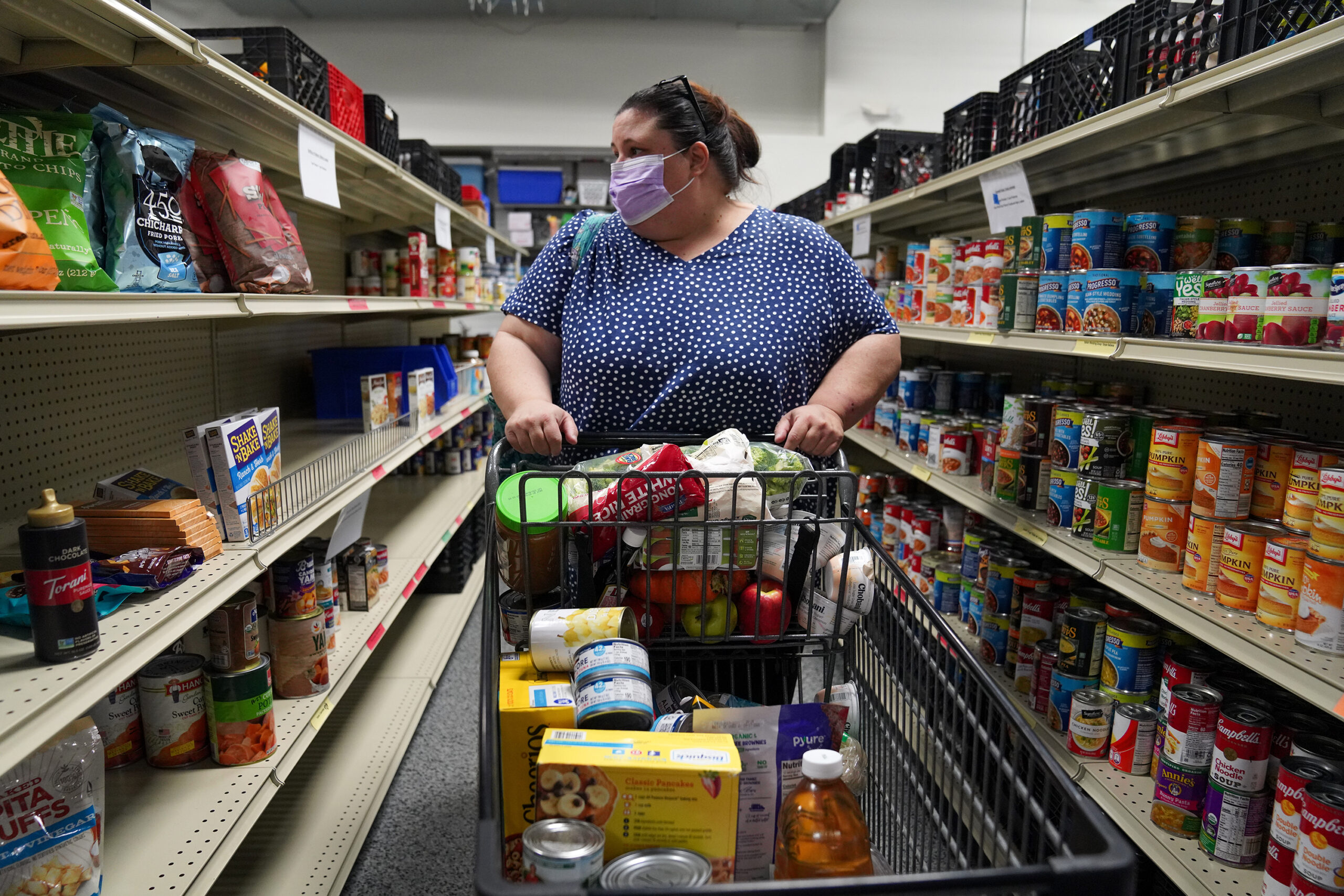 A woman in a mask pushes a card down an aisle at a grocery store