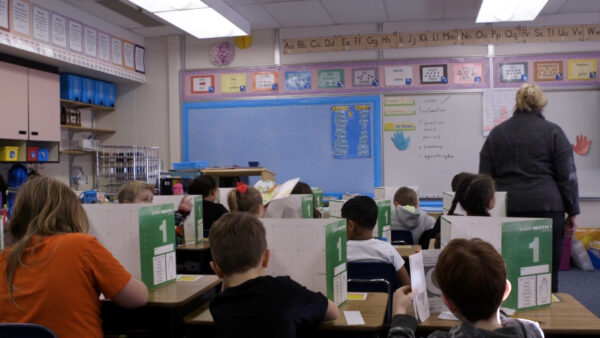 Students sit behind desks with privacy folders up in an elementary school classroom.