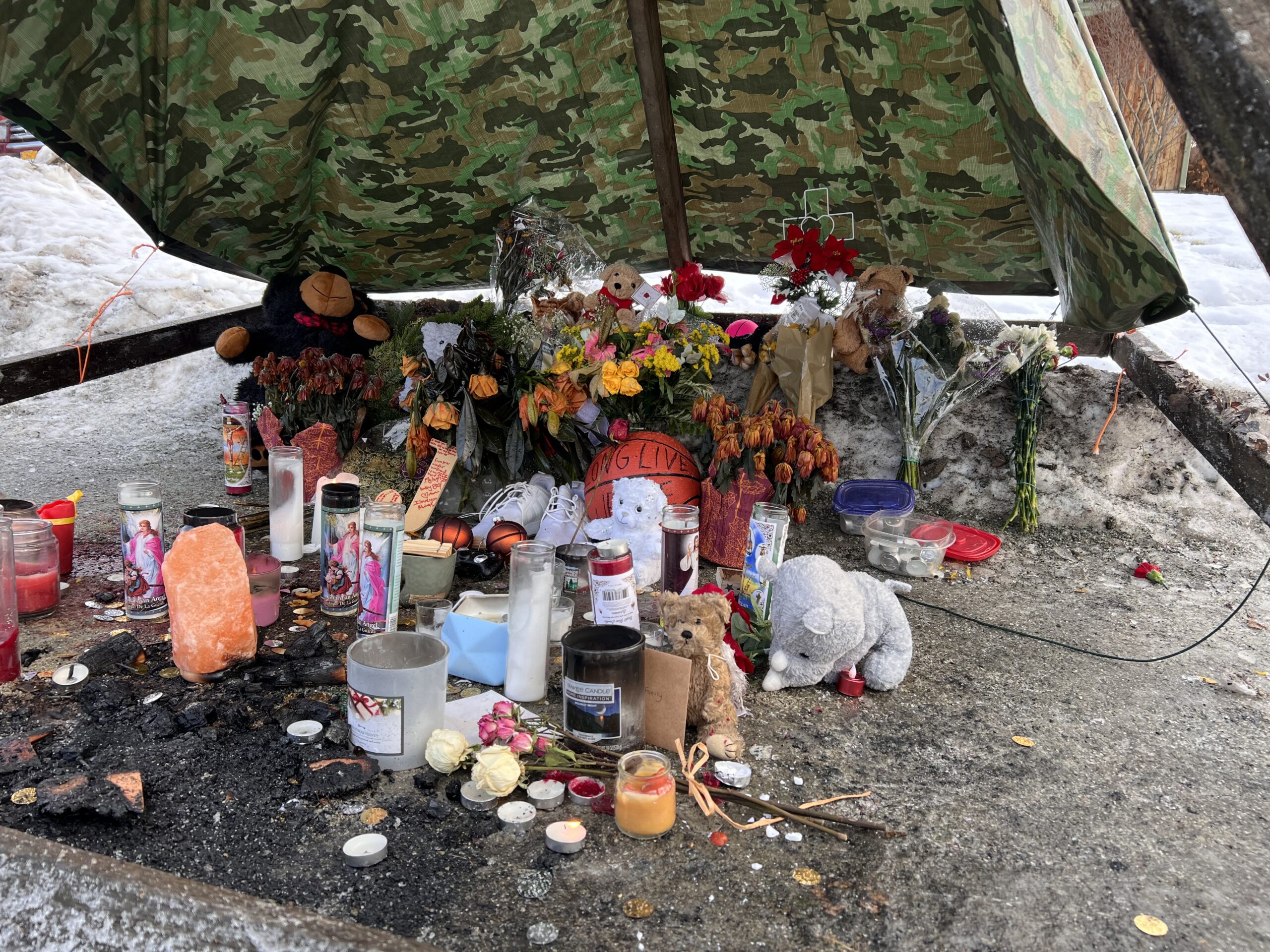 a memorial with stuffed animals and flowers under a tarp, on an icy road