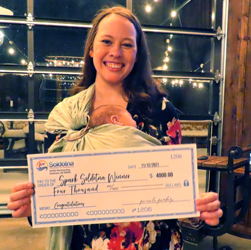 a woman holds a baby and a $4,000 check