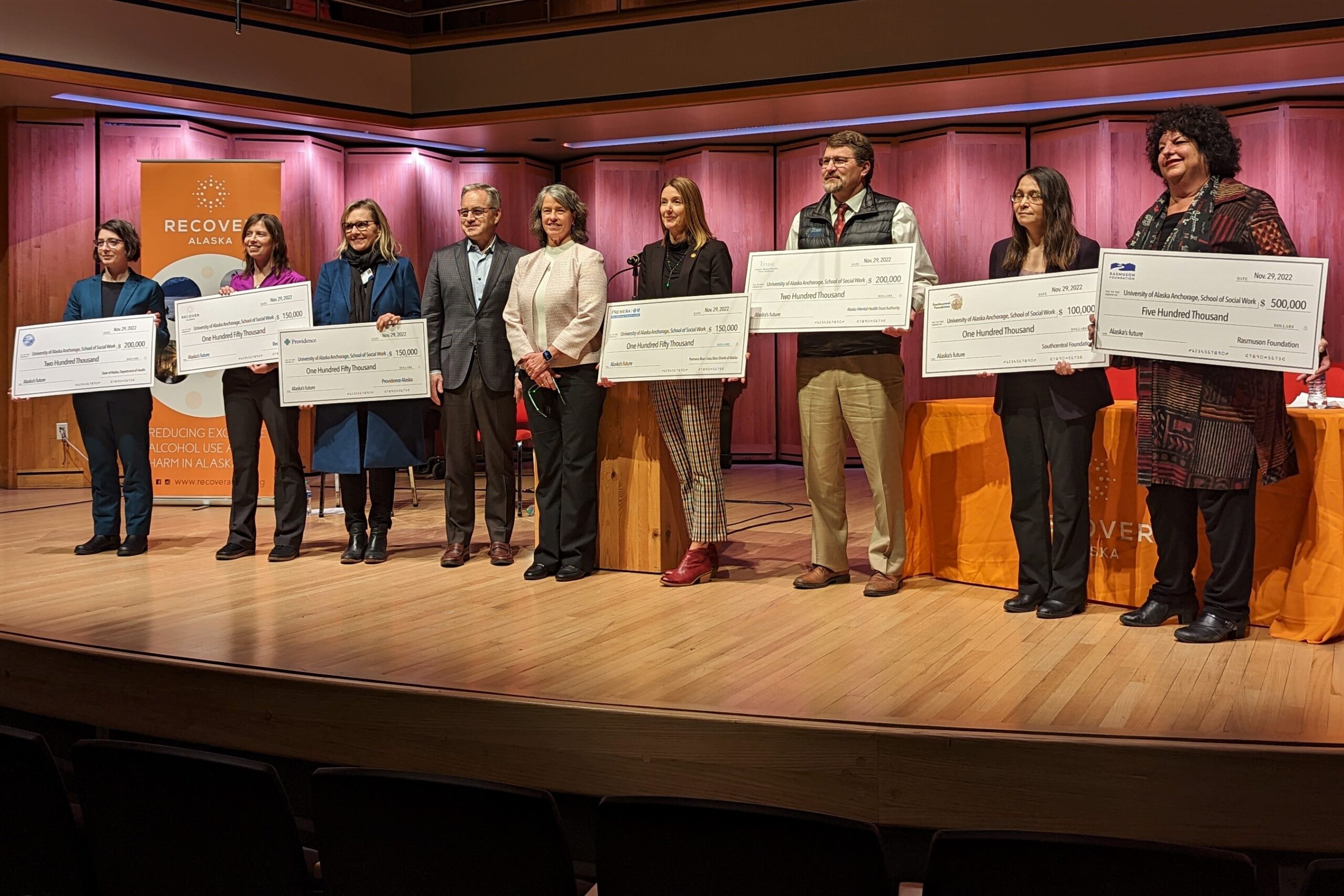 Representatives of various institutions that pitched in for a $1.5 million grant to the University of Alaska Anchorage’s School of Social Work pose for photos with oversized checks during a press conference