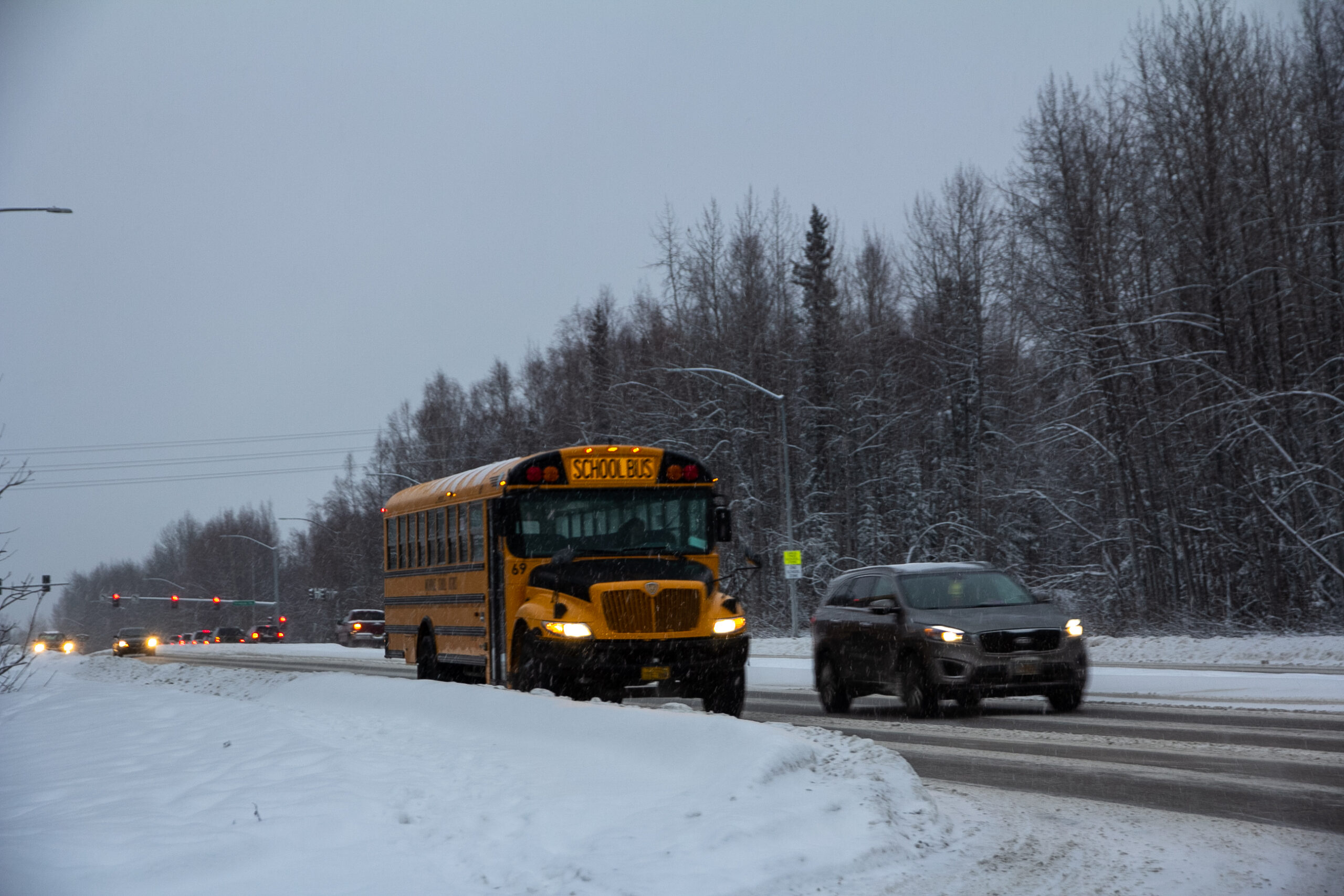 A school bus and an SUV drive on a snowy road under an overcast sky.