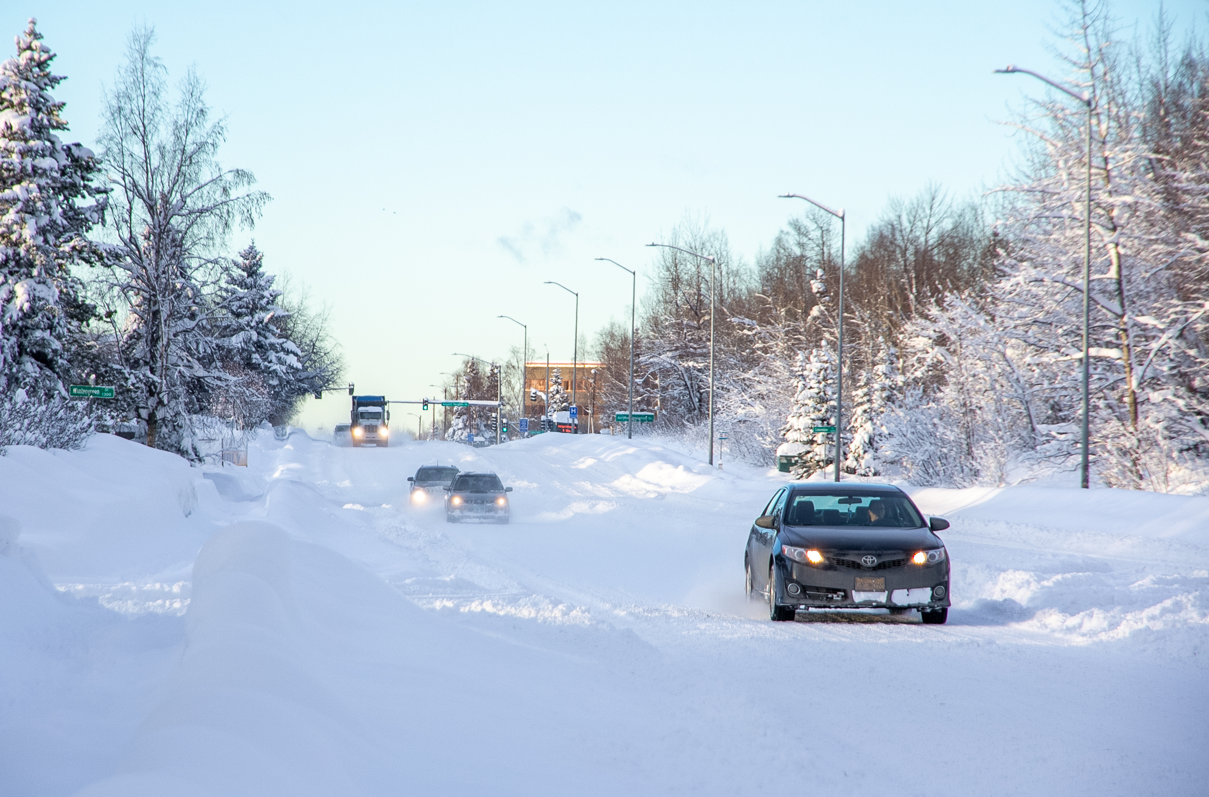 Cars drive on a snow-covered road on a sunny day.