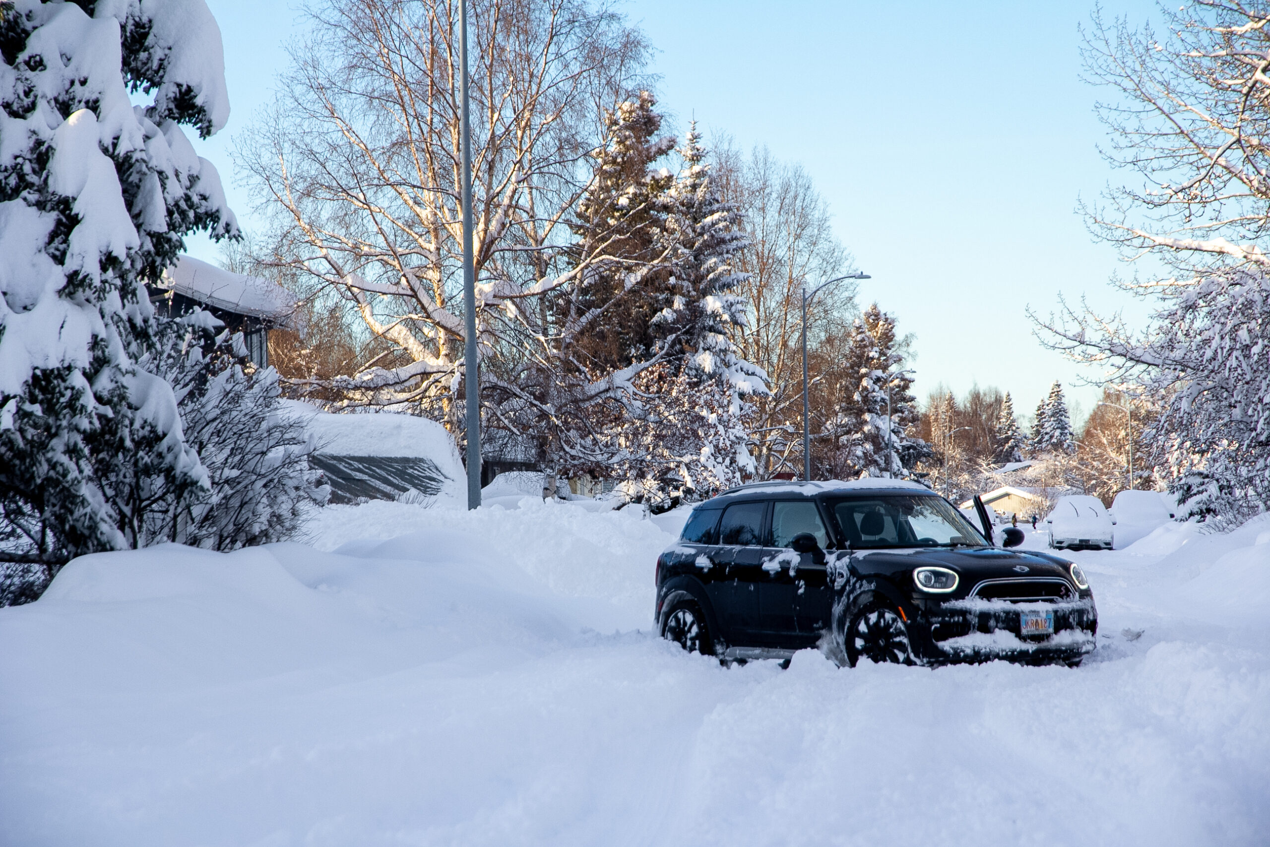 A Mini Cooper sits stuck in snow in the middle of a residential road.