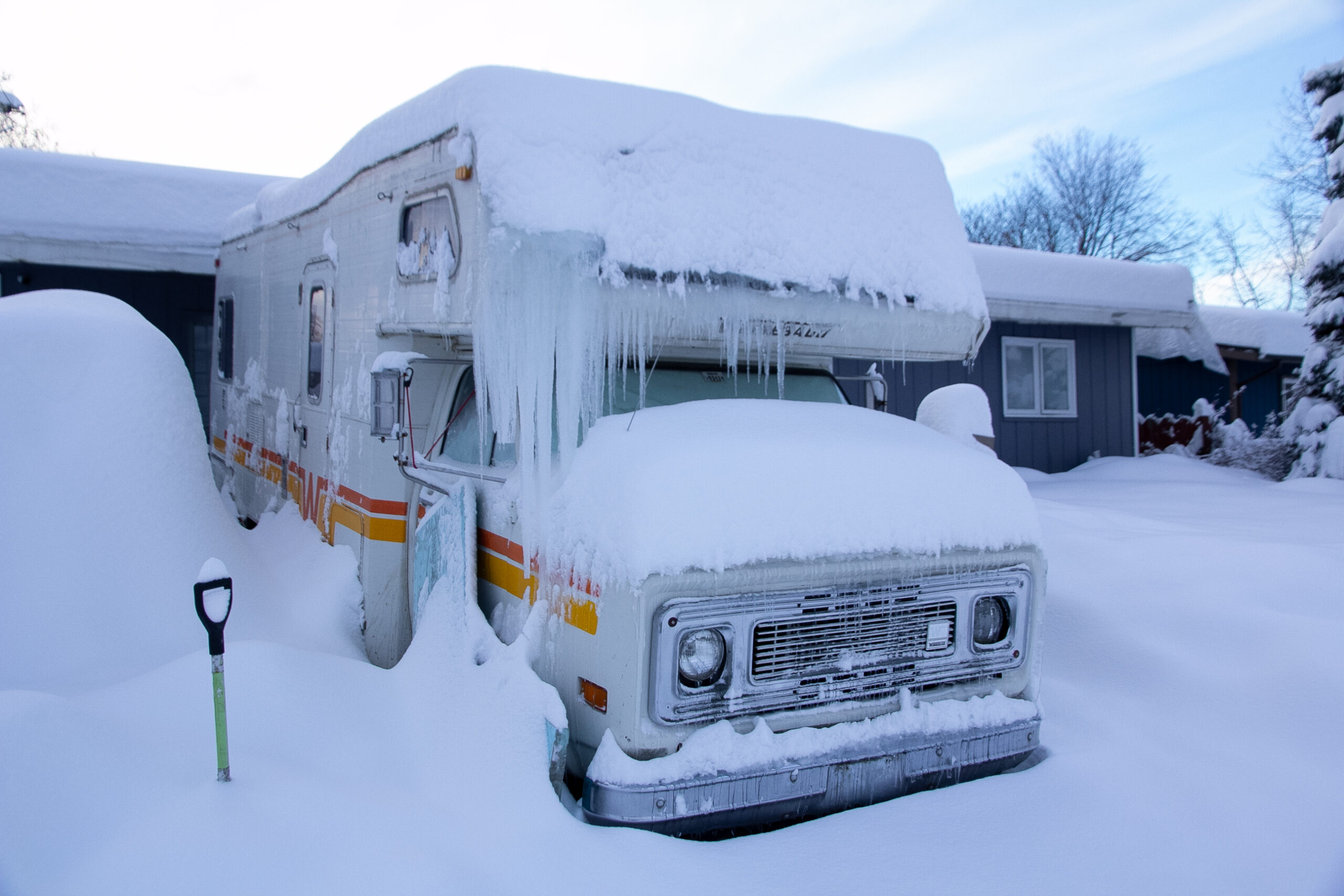 An RV is covered in snow and icicles hang from the roof.