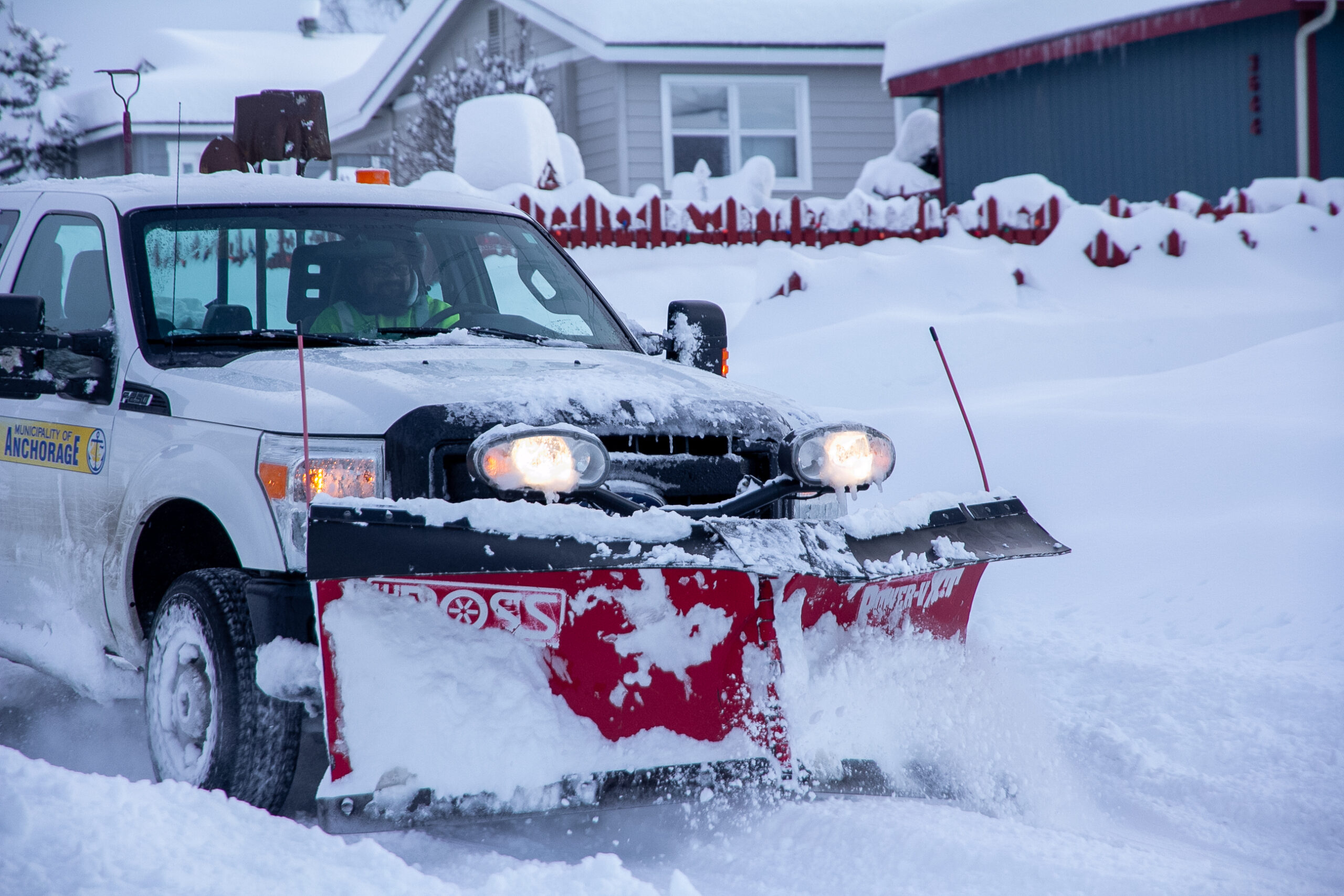 A snowplow pushes through thick snow on a residential street.