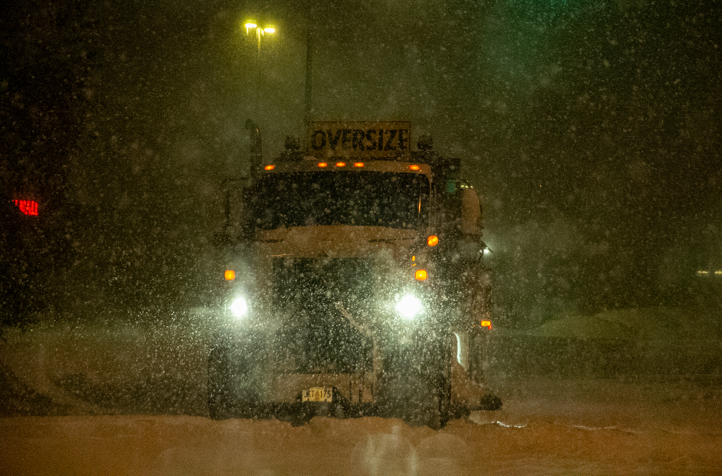 A large truck drives through a heavy snowfall.