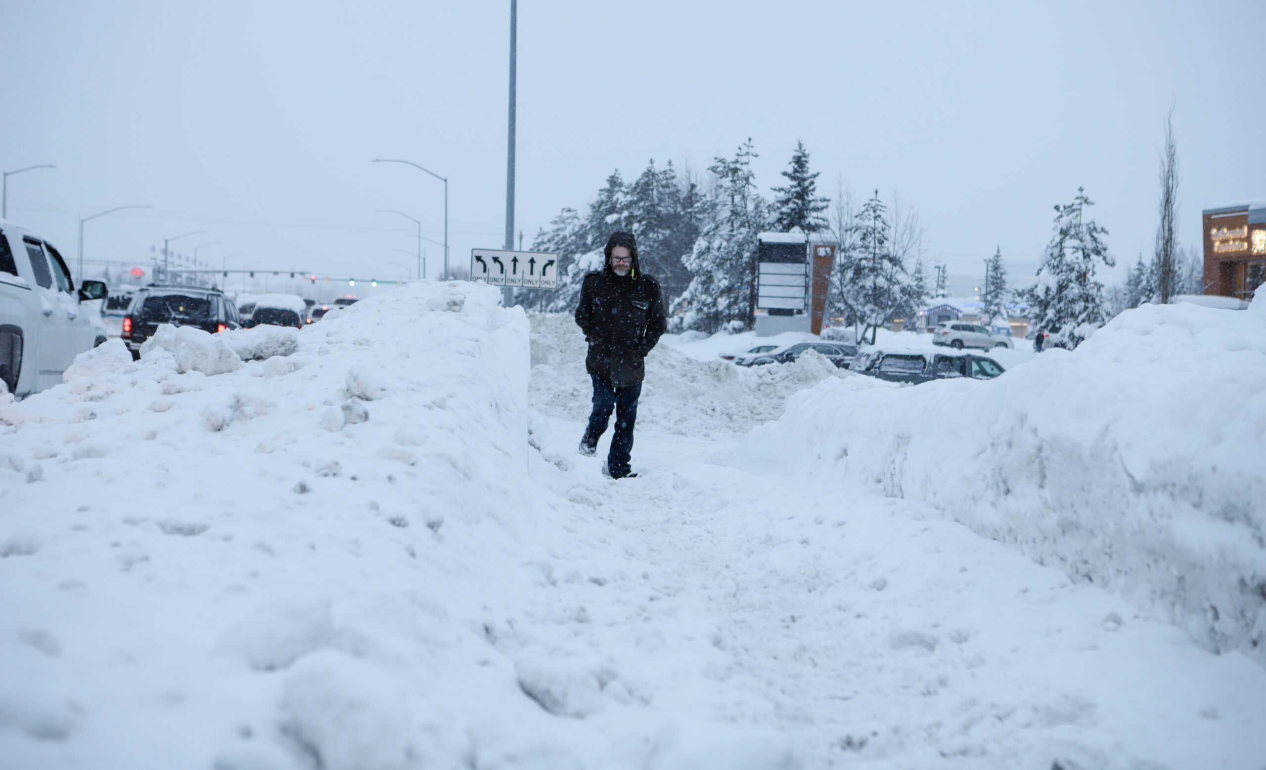A man in a black coat walks on a snow roadway.