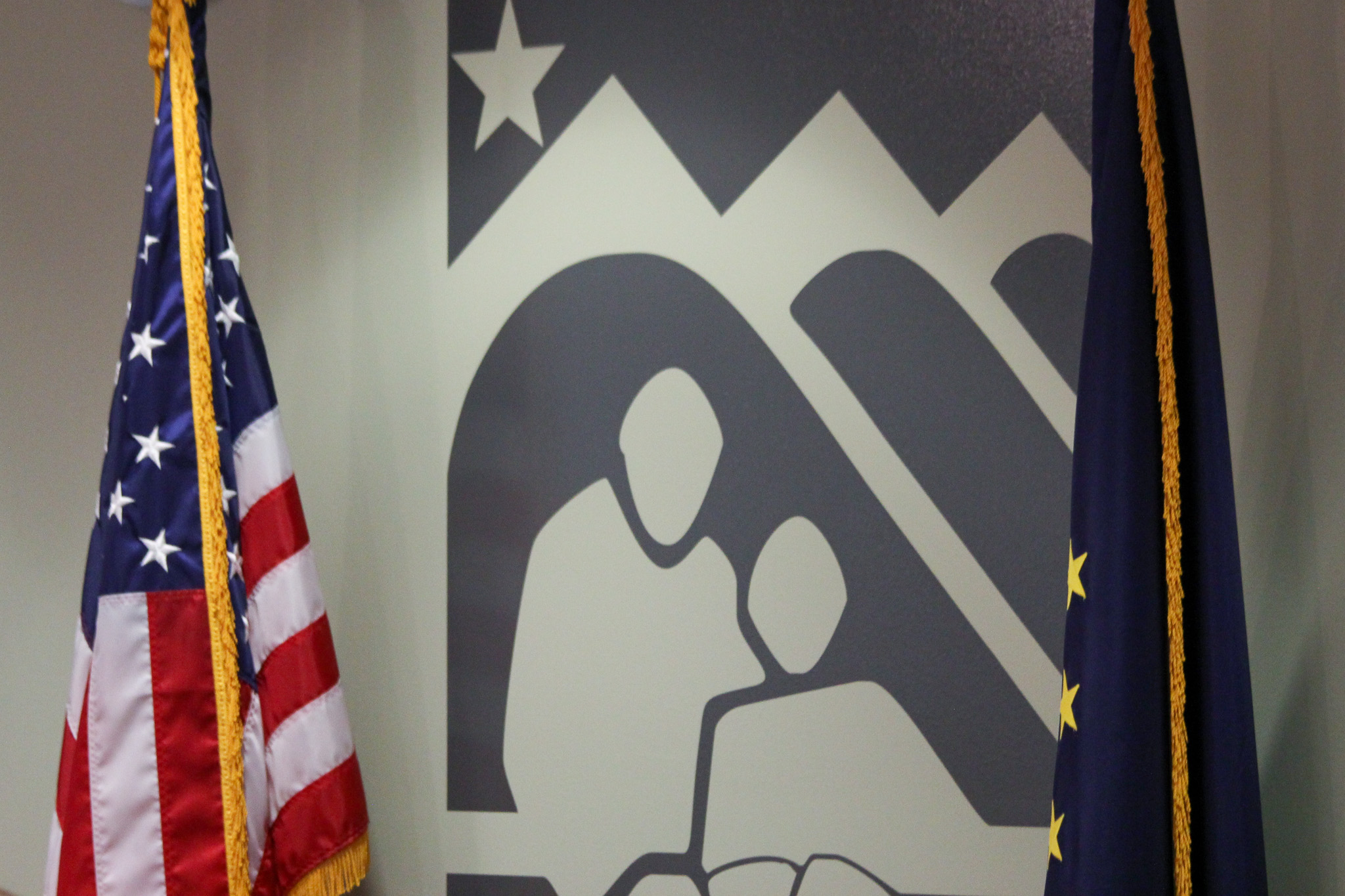 A logo is painted on a wall between the Alaskan and American flags.