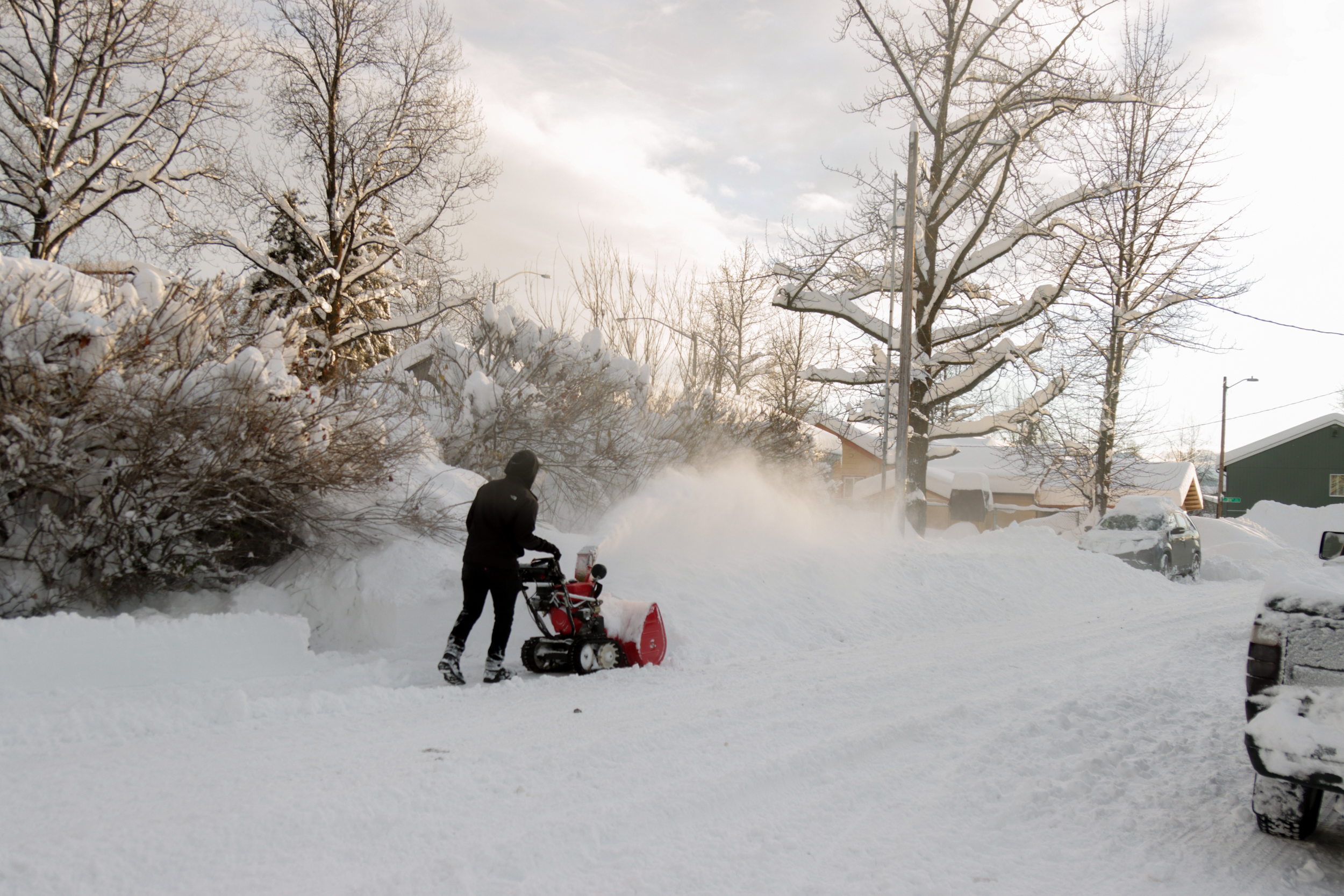 A person uses a red snow blower.