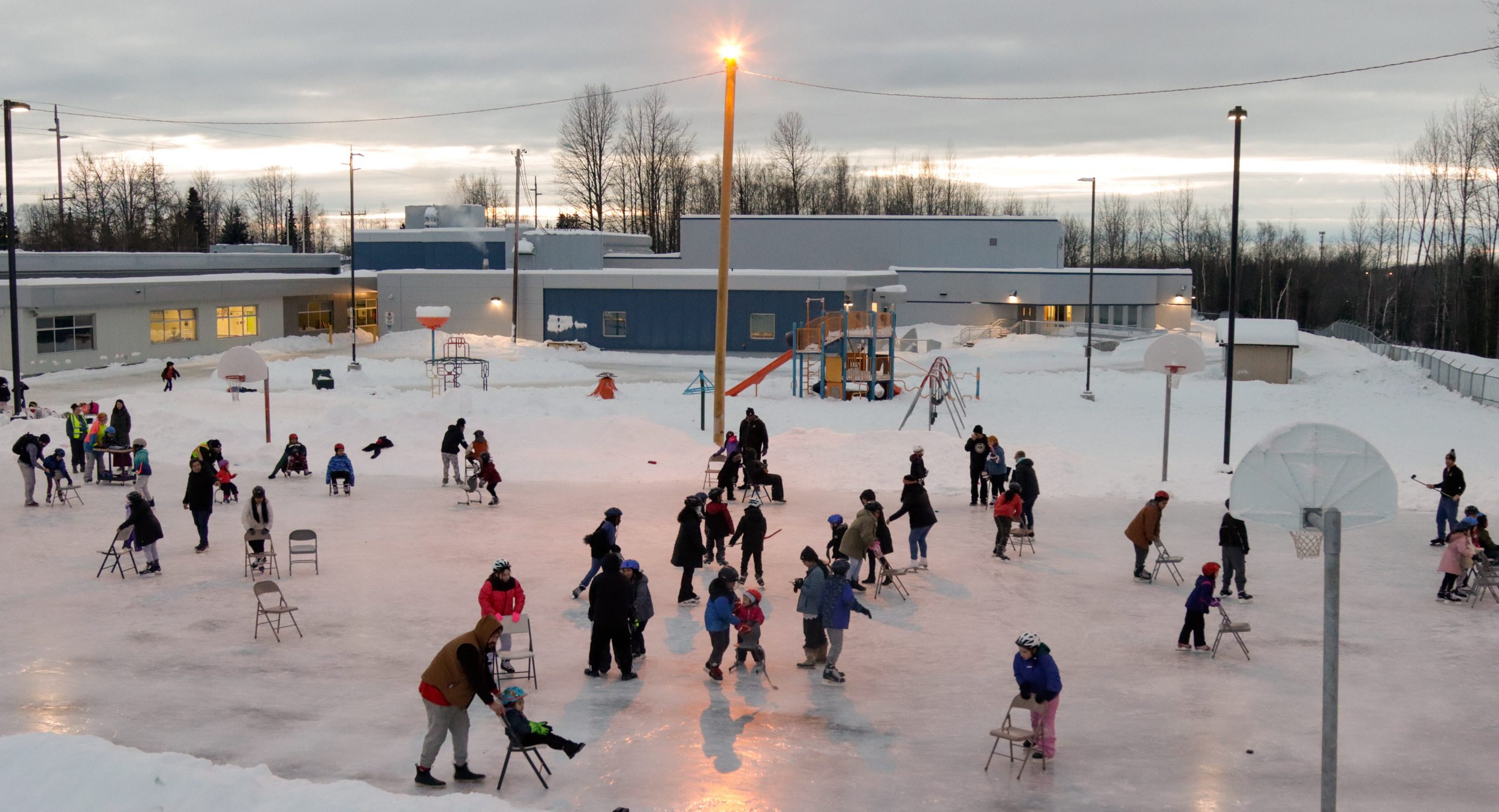 A crowd skates on an ice rink on a school basketball court.