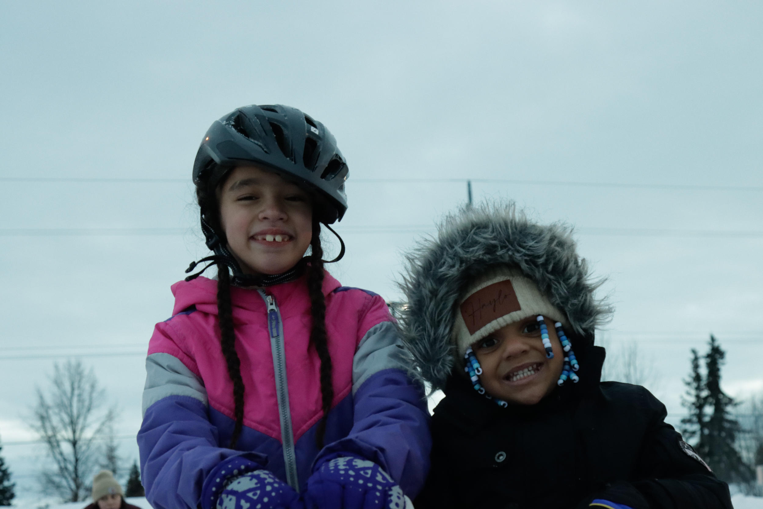 Two young girls pose for a photo in snow gear and helmets.