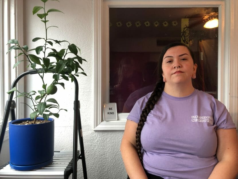 a woman in a purple t-shirt poses for a photo next to a houseplant