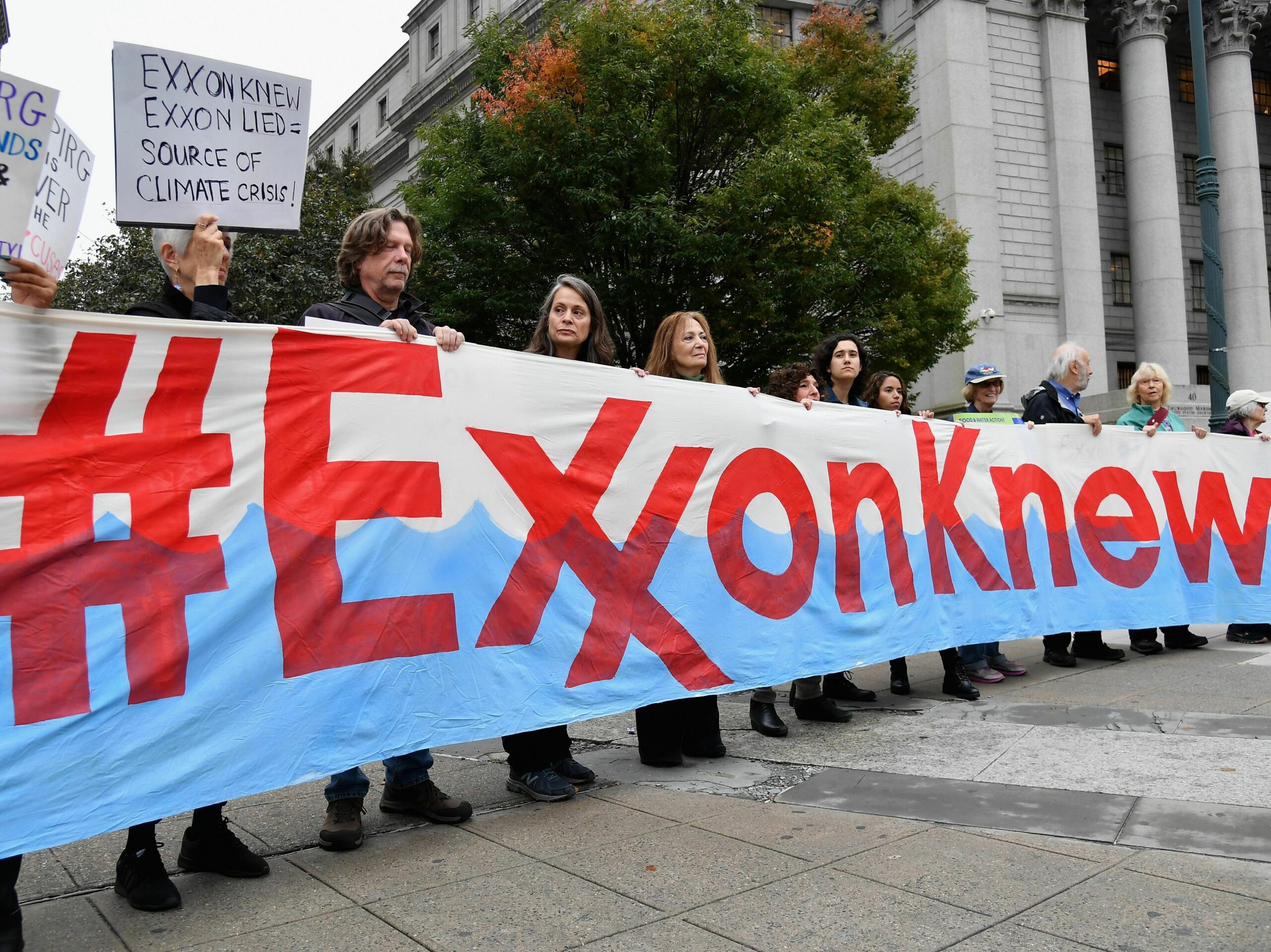 a line of people hold a banner that says #ExxonKnew