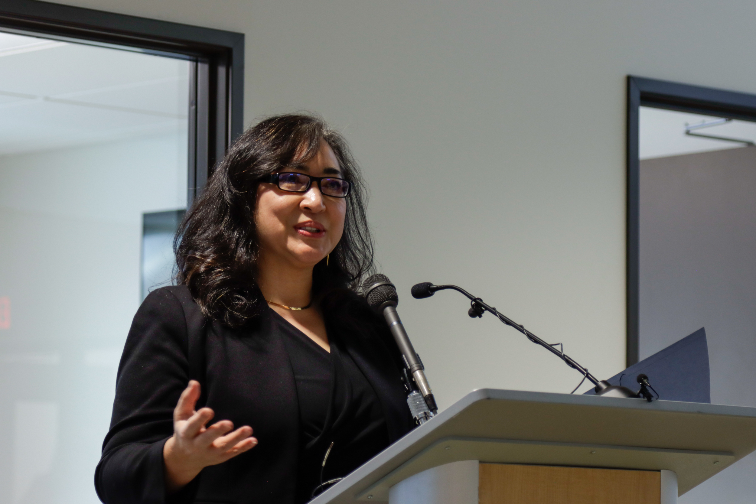 A woman in glasses speaks behind a podium.