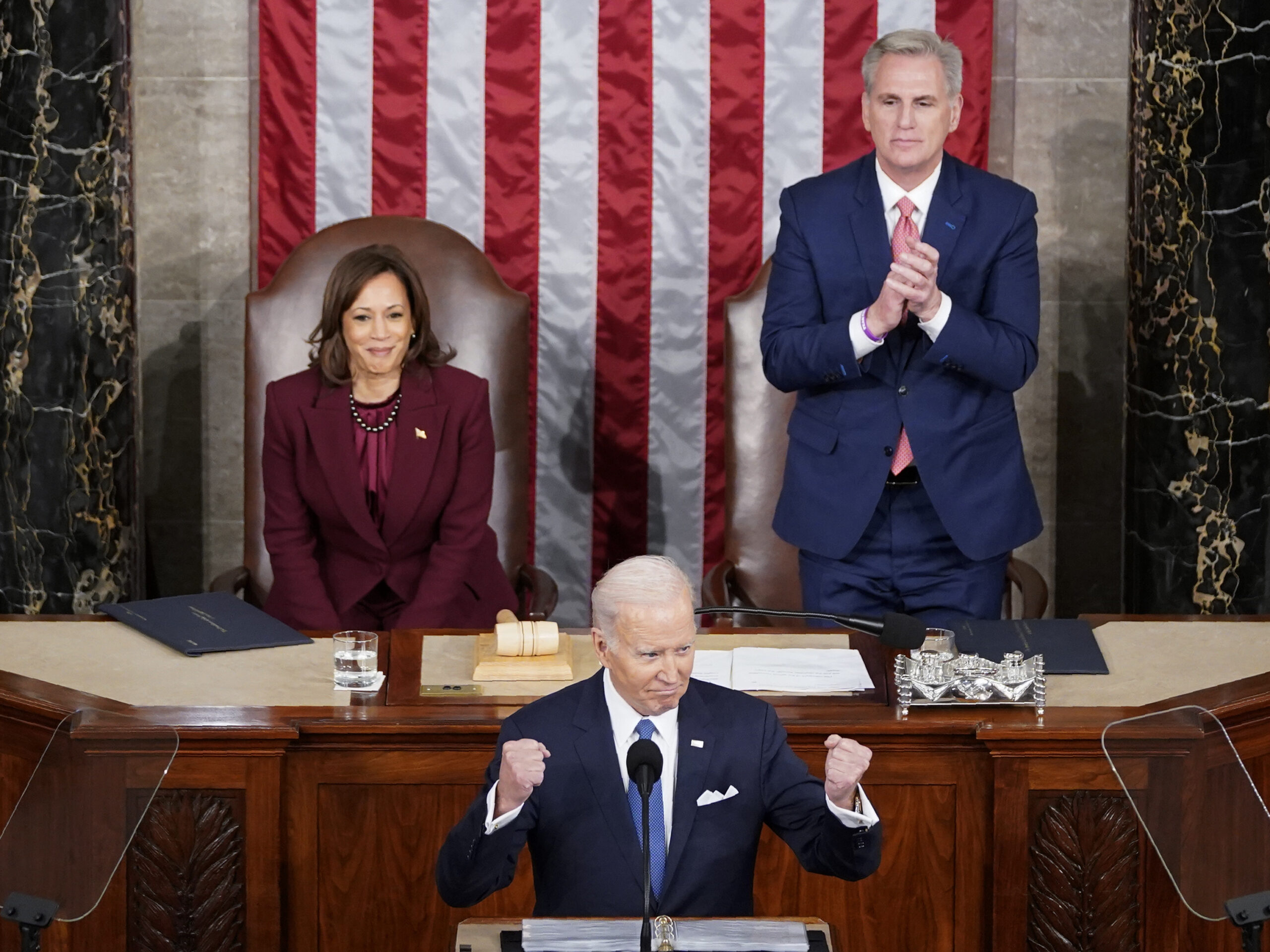 three people at desks, with the american flag in the background