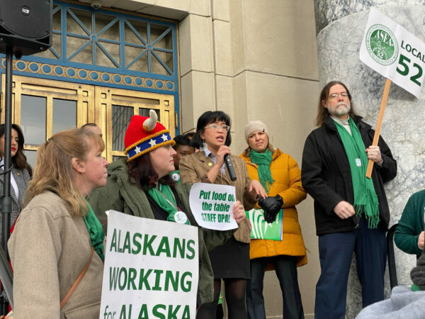 People stand on the steps of a building, with signs that say: Alaskans Working for Alaska