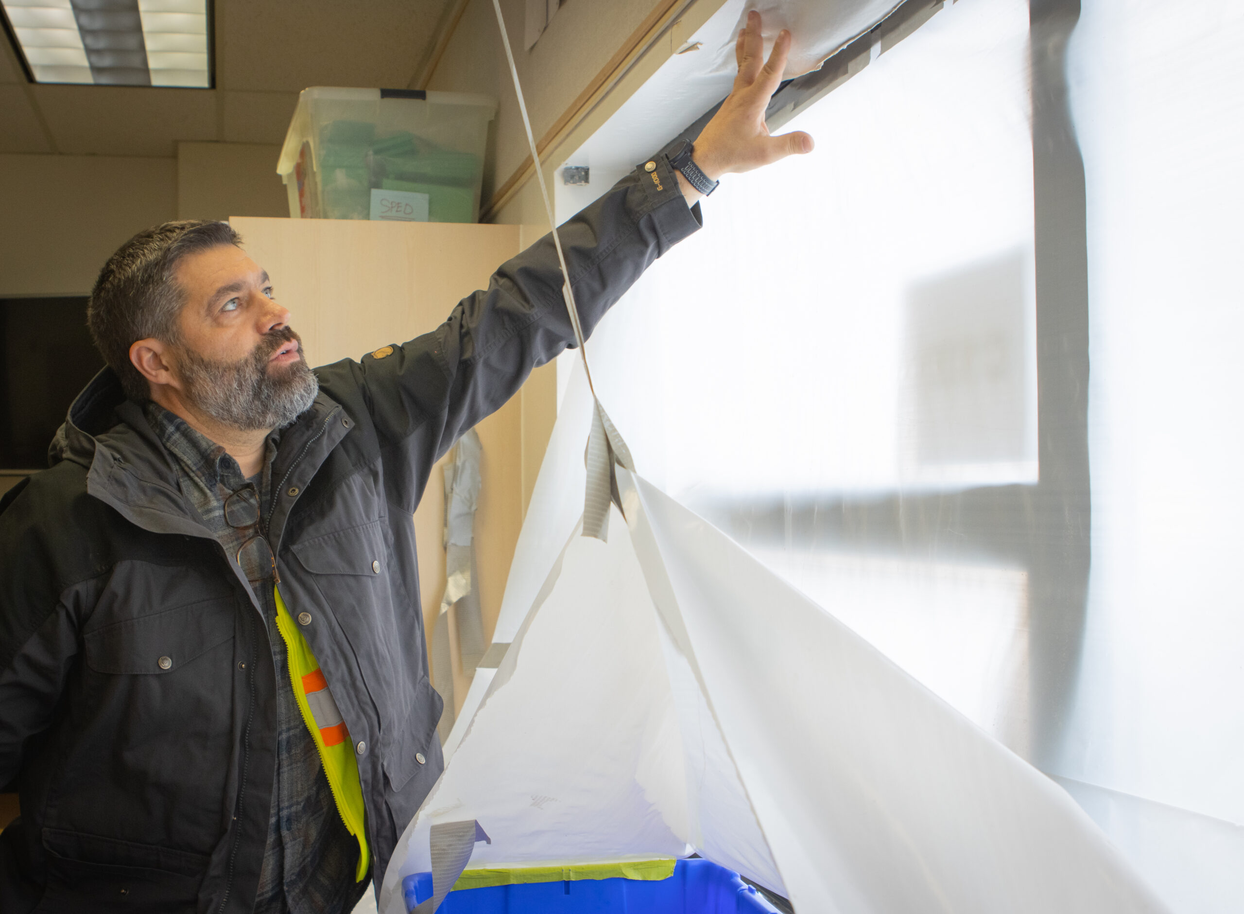 A man in a dark jacket examines a damaged window.