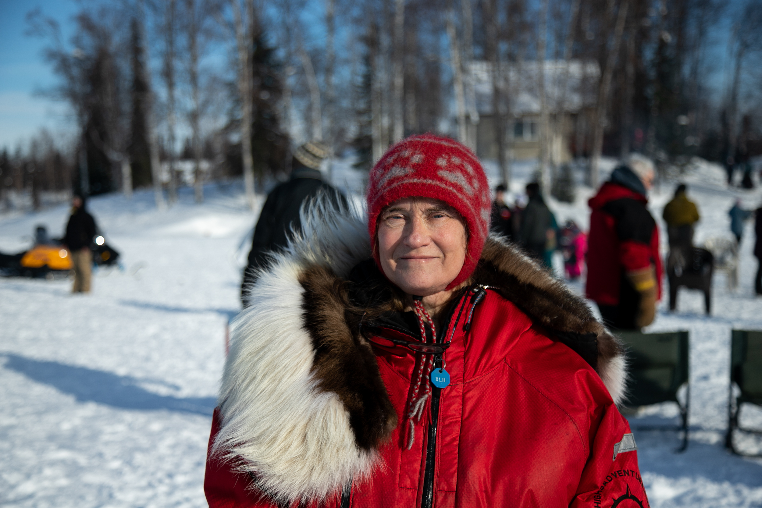 A woman wearing a red hat and red parka poses for a photo on a frozen lake.