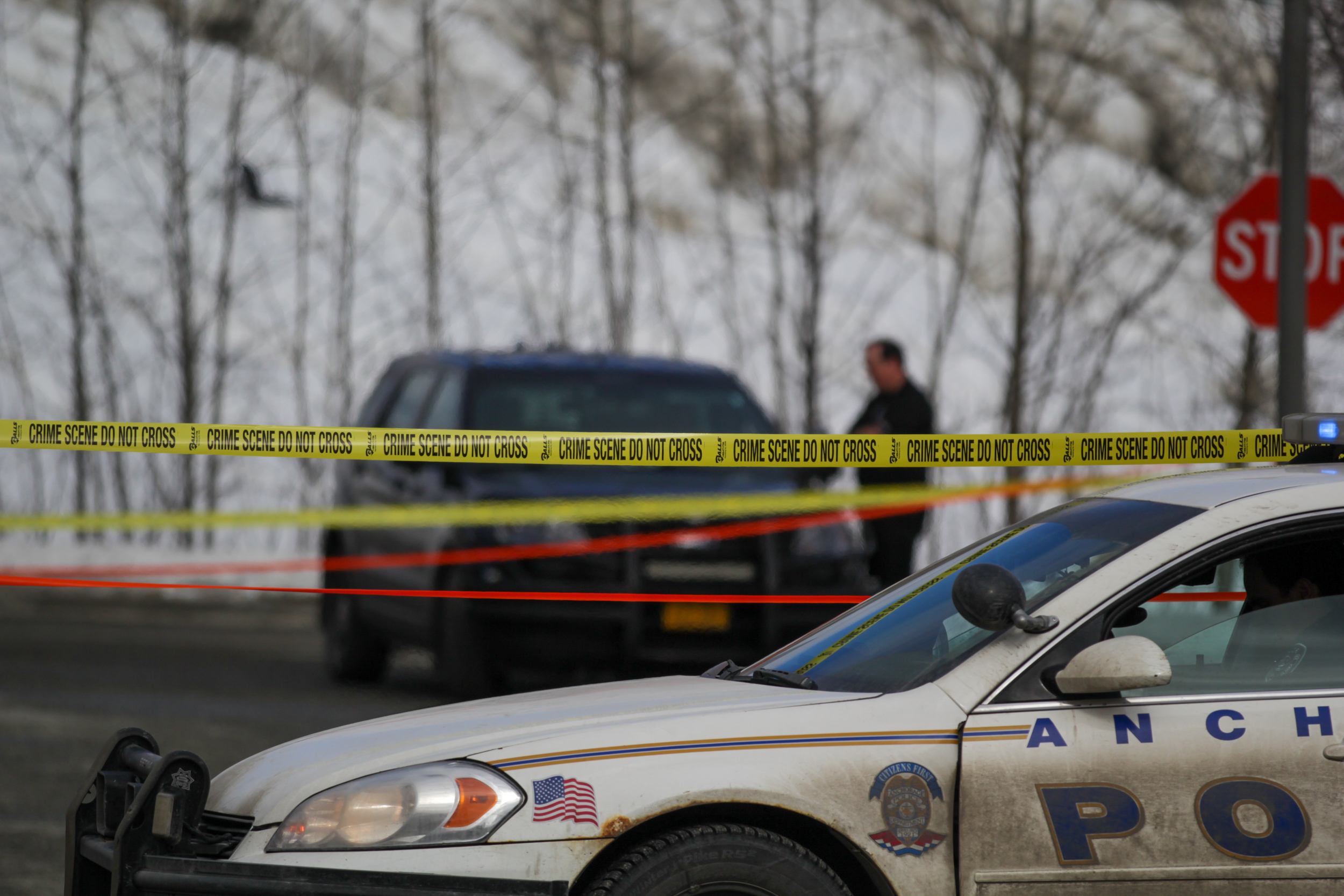 A cop car sits in front of crime scene tape in a parking lot.