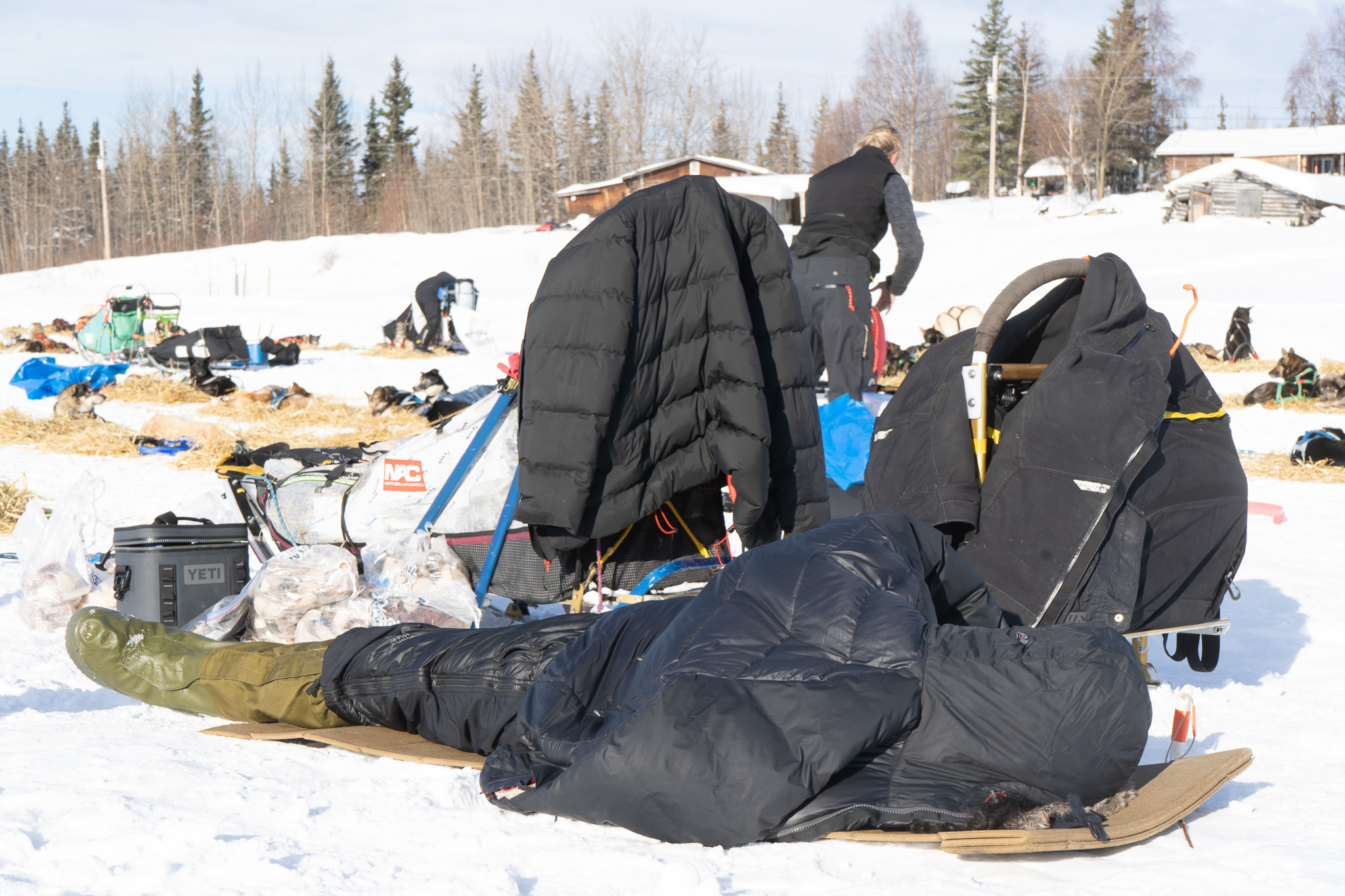 A person lies on a camping mat next to a dog sled