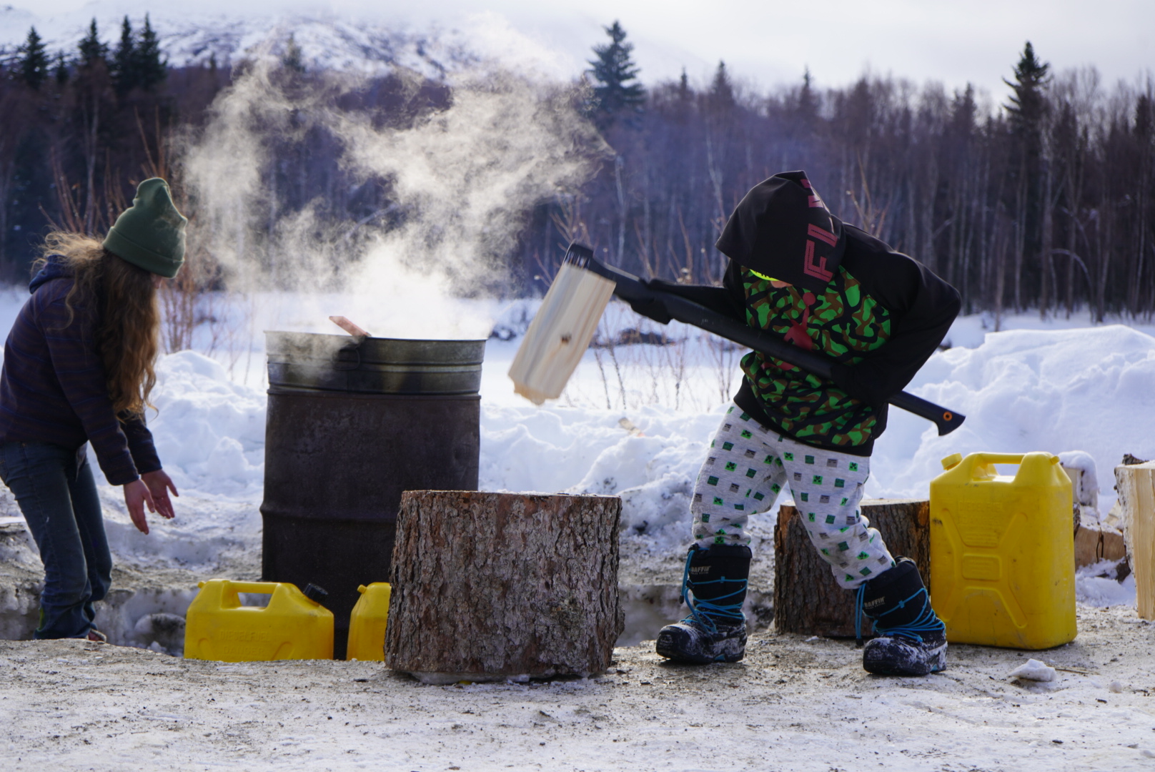 A kid chops wood in front of a burn barrel
