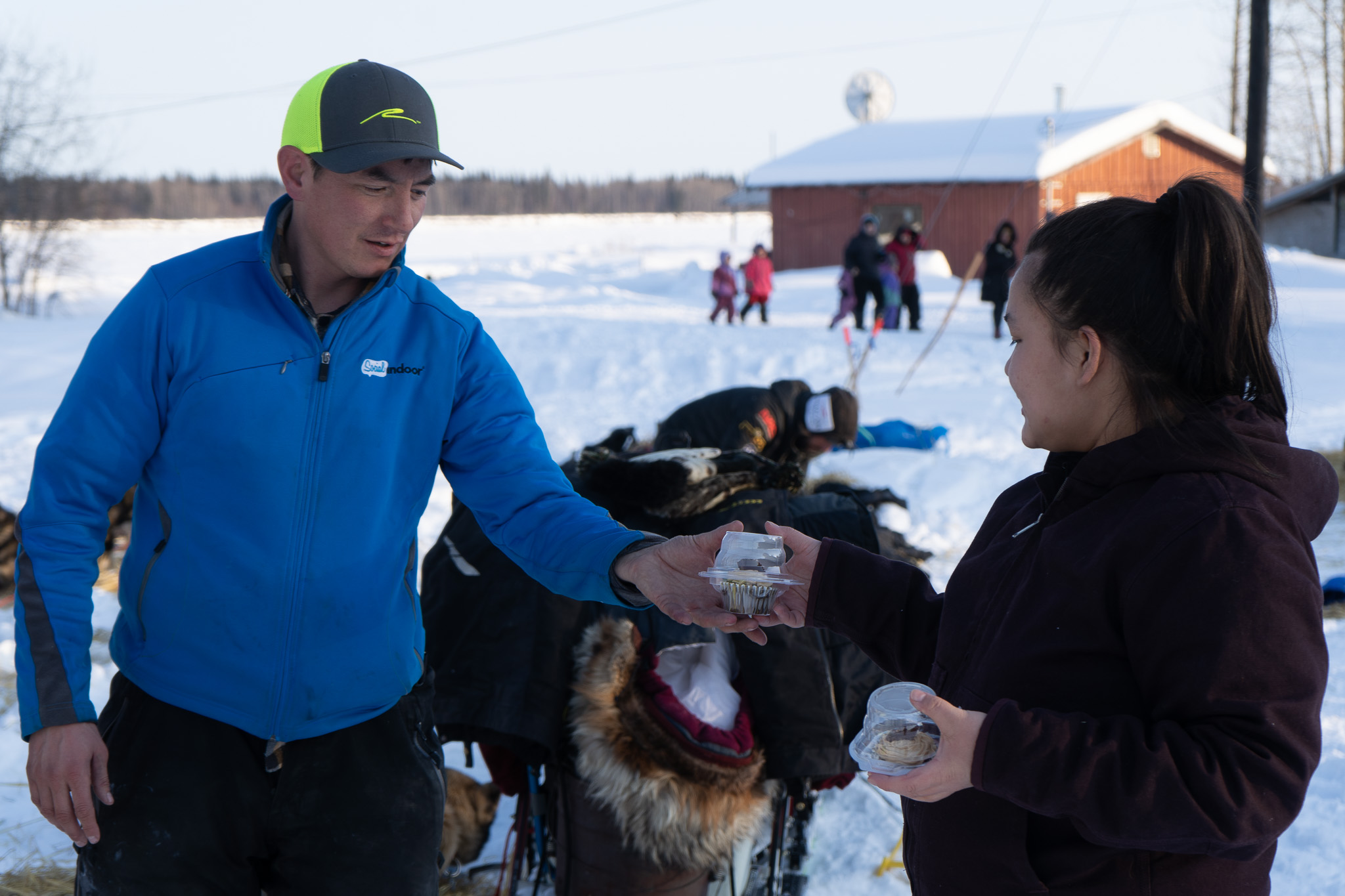 A person passes a plastic cupcake to a musher in a baseball hat