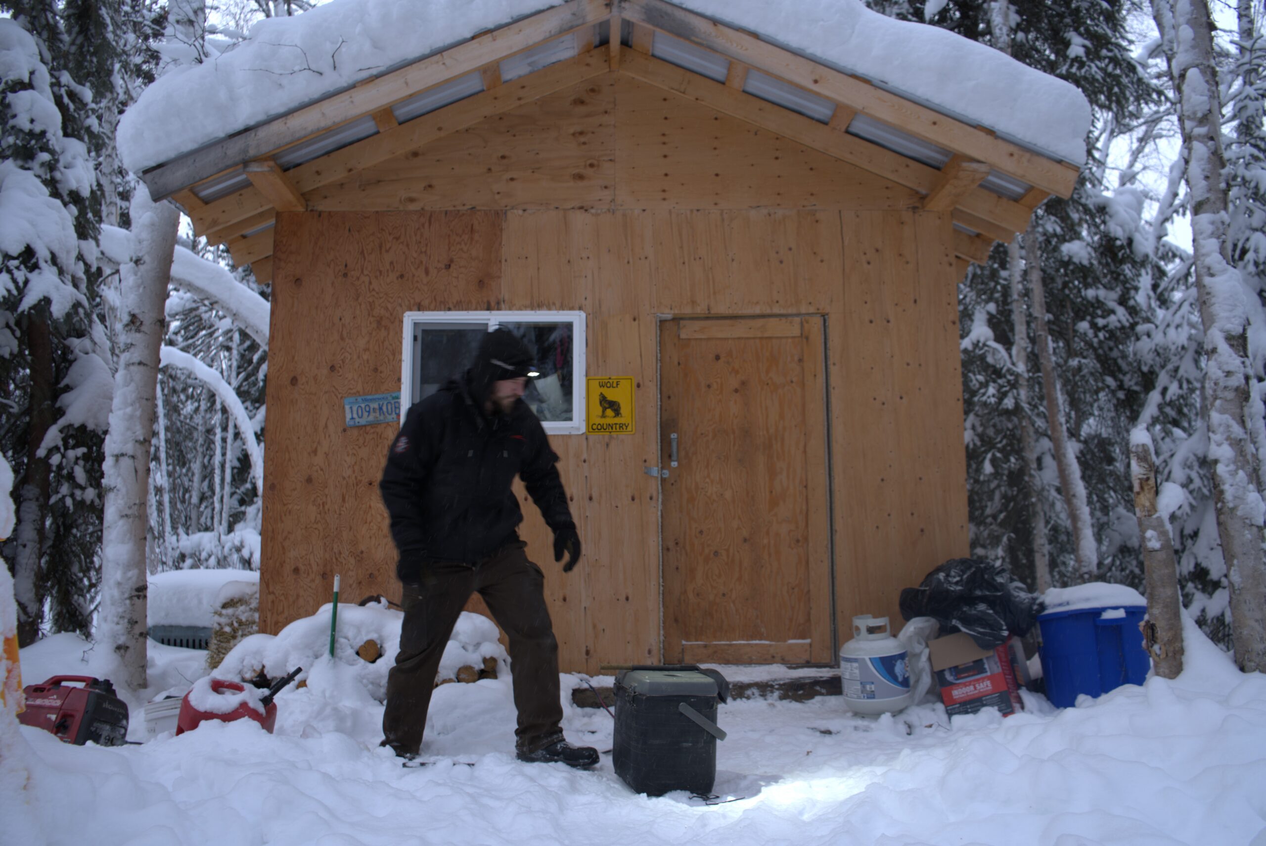 A man in front of a plywood cabin 
