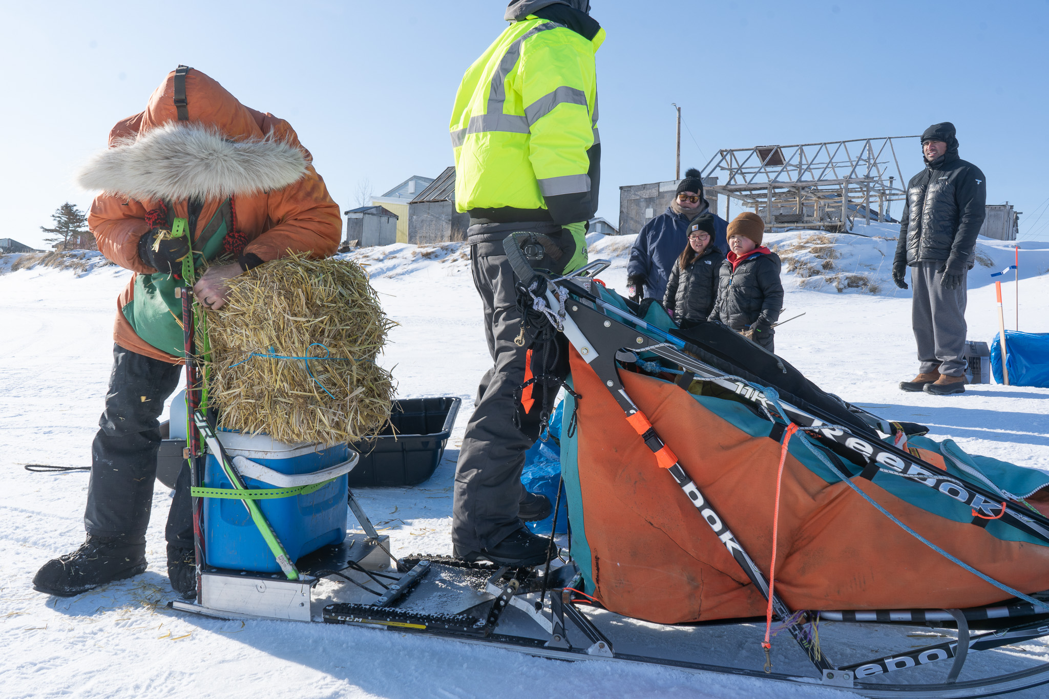 People watch as a musher ties straw to his sled
