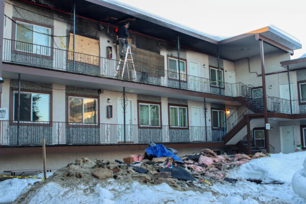 Debris fills the yard of a burnt apartment building while a man stands on a ladder.