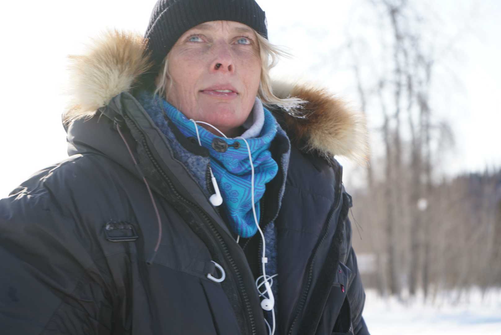 a woman in outdoor gear, with headphones hanging from her jacket