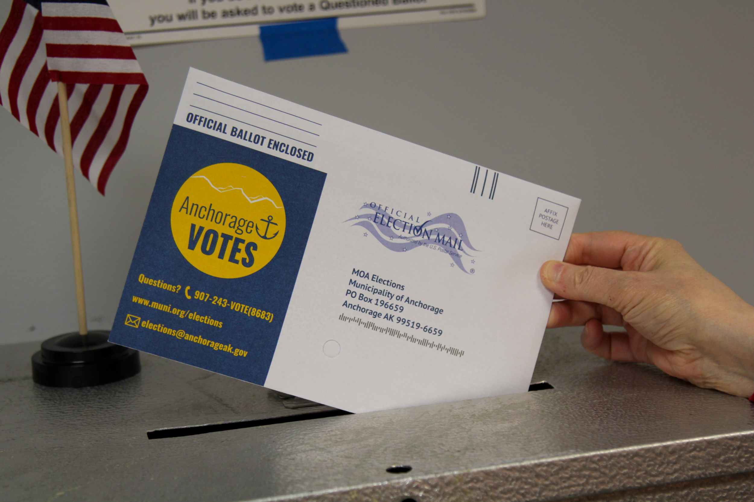 A hand places a paper ballot in a ballot box.