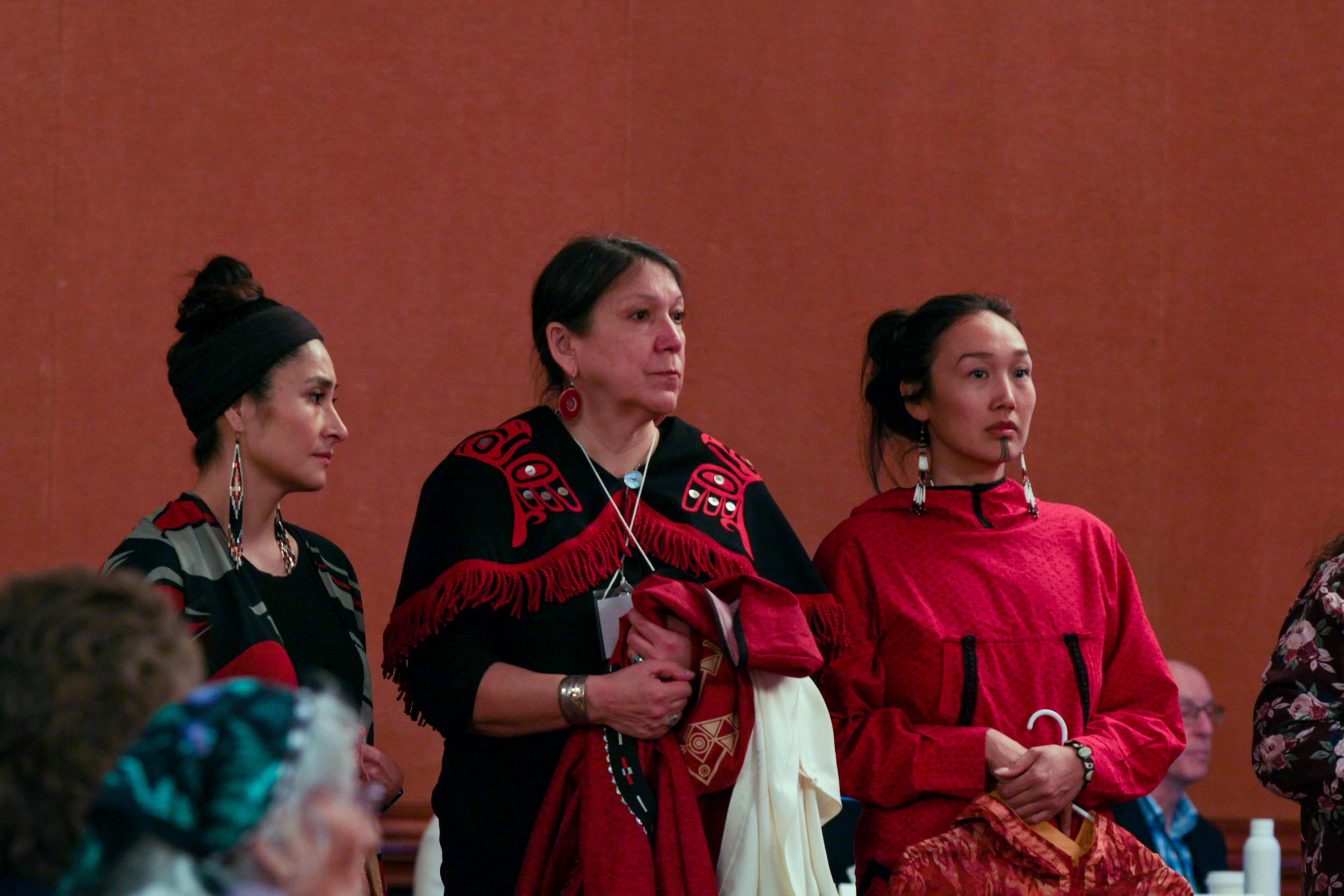 Three women holding Alaska Native regalia,