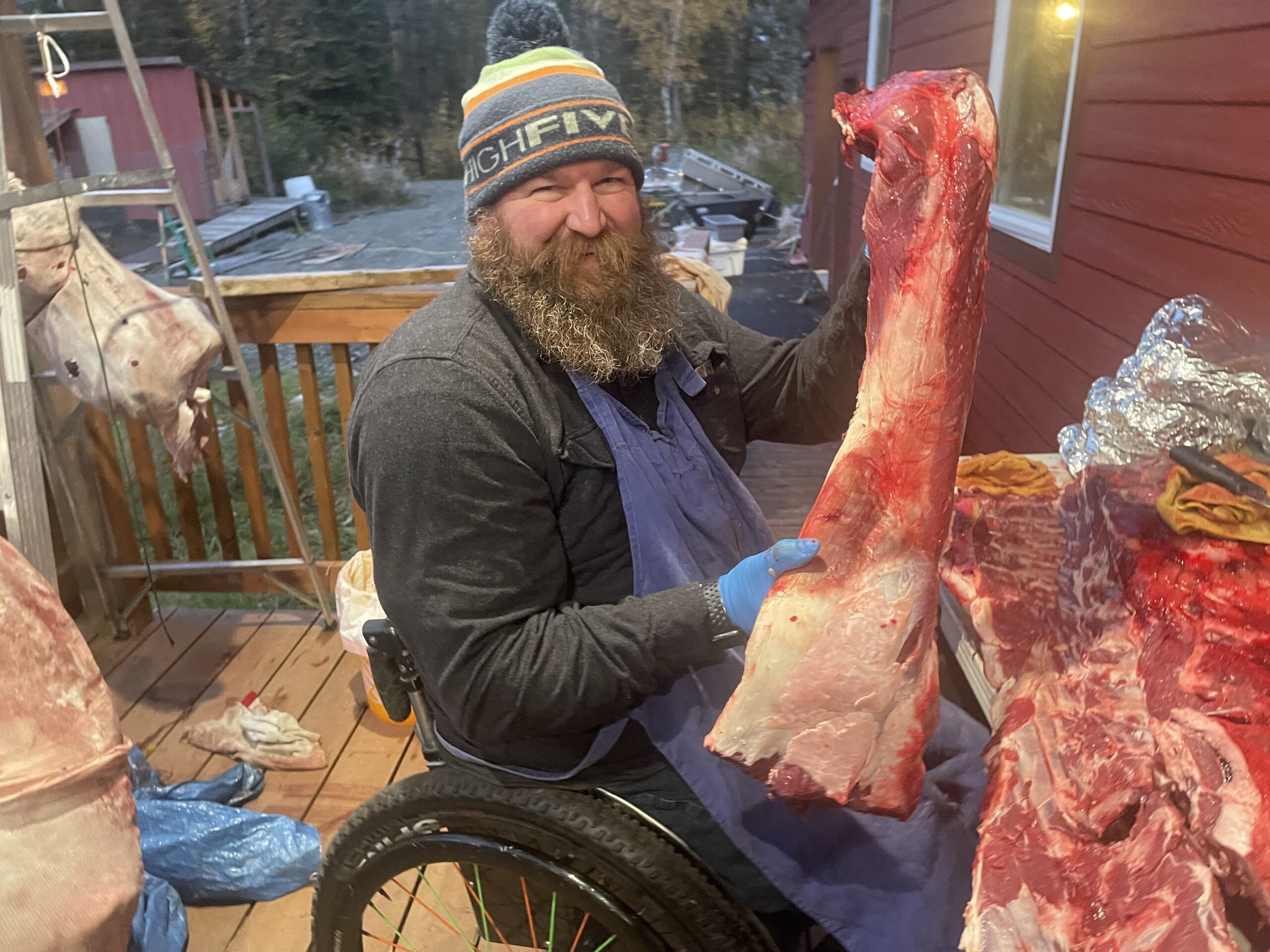 A bearded man in a wheelchair holds up a piece of meat.