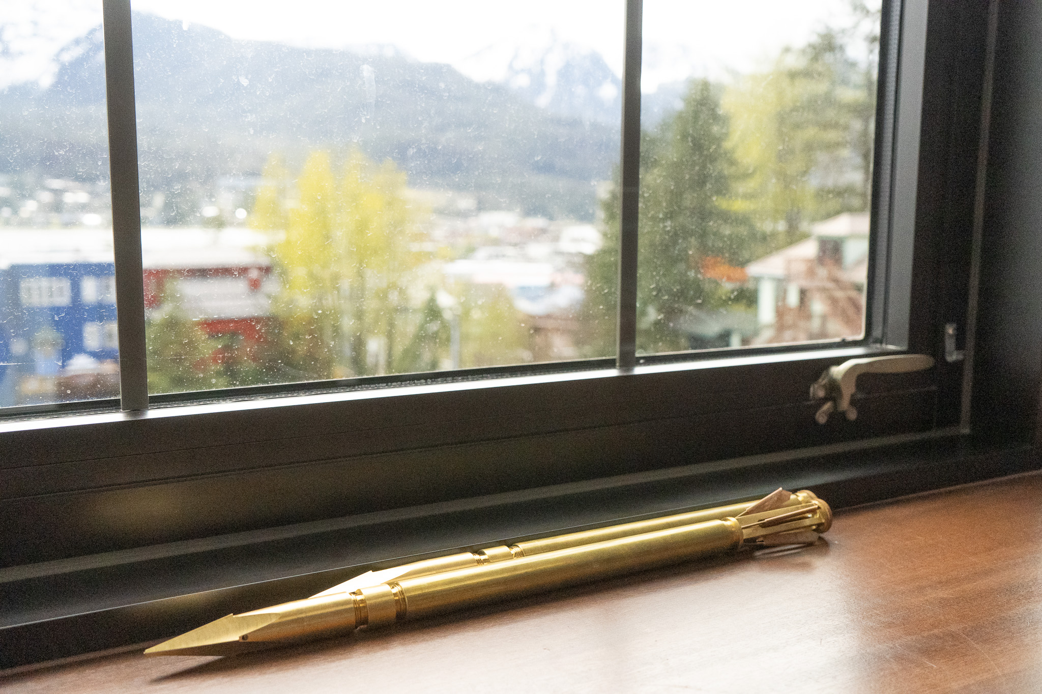 A gold colored harpoon tip case on a windowsill with snowy mountains in the background