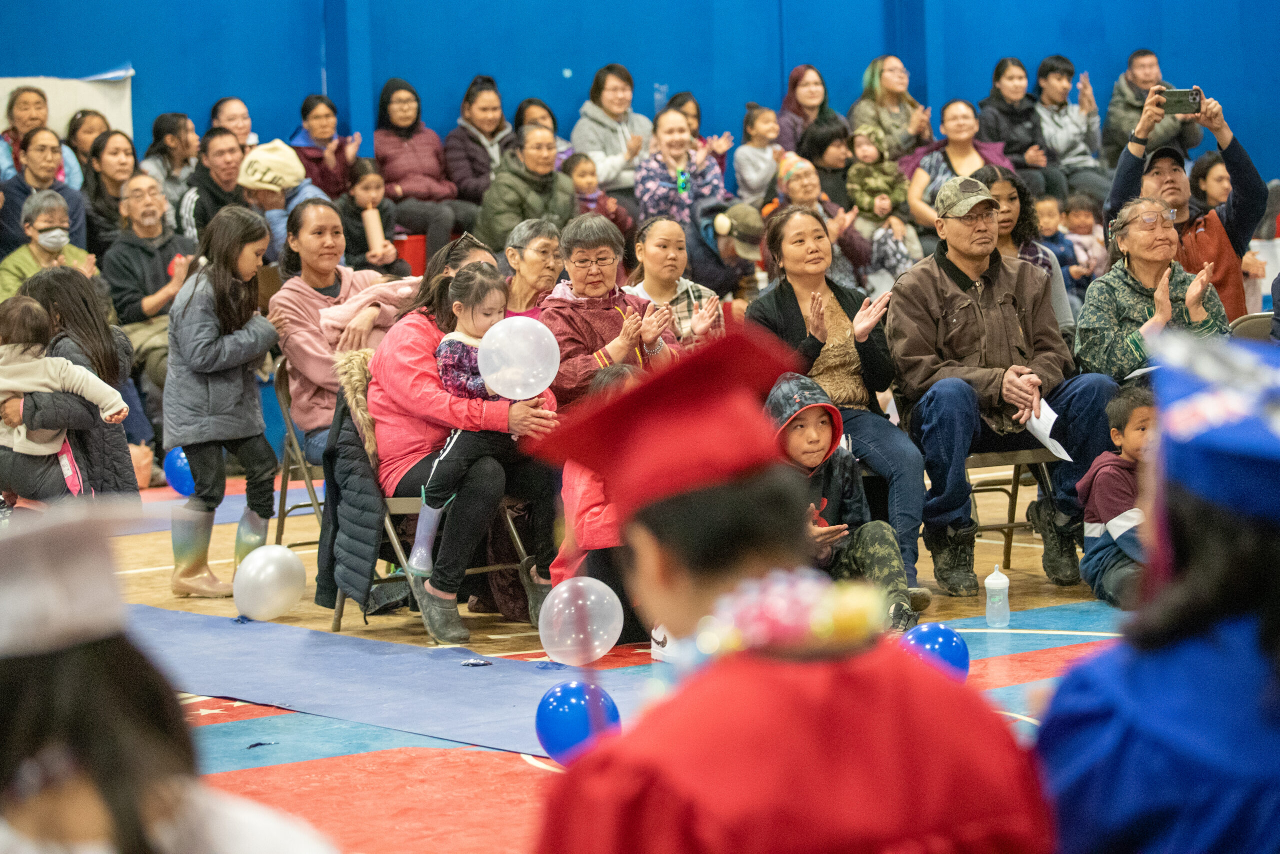 A gymnasium full of people applaud graduating high school seniors.