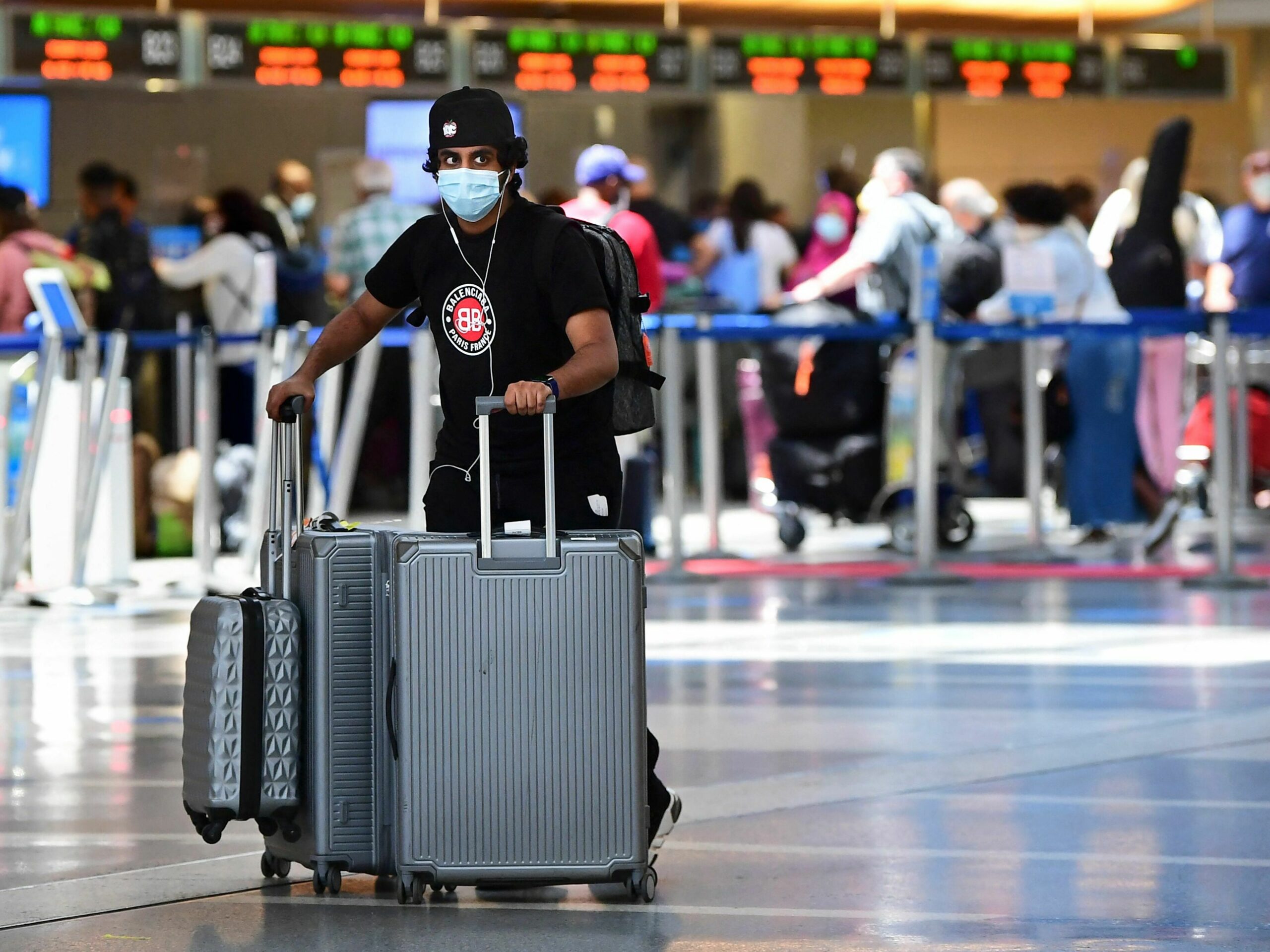 a man pushes his suitcases, wearing a mask, in the airport