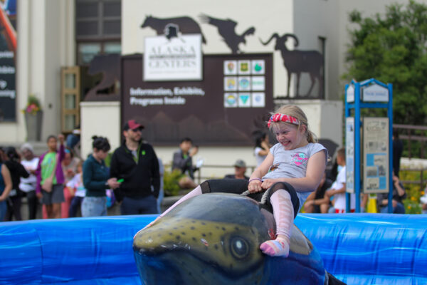 A girl rides on a mechanical salmon carnival ride.