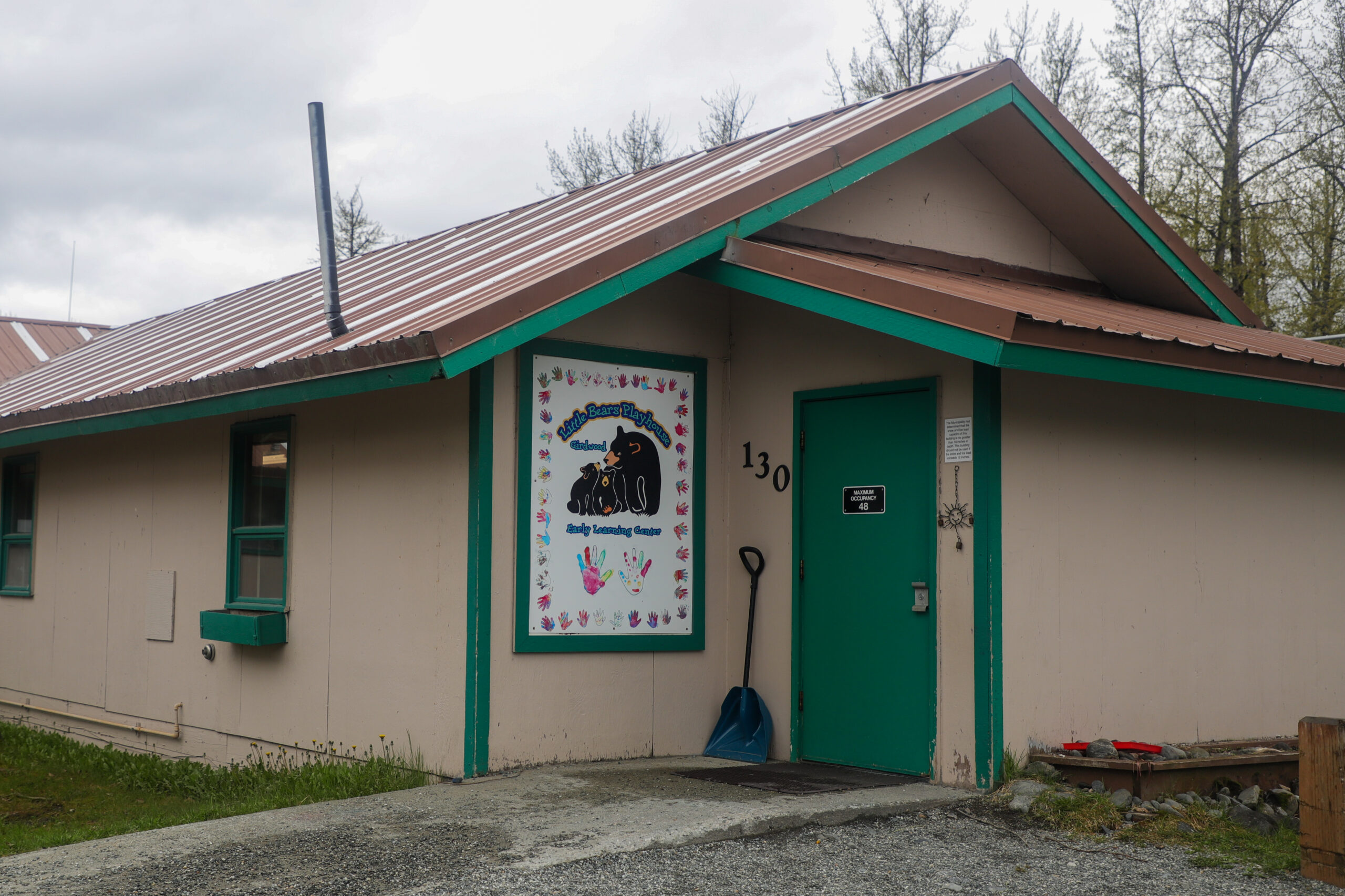 A brown building with a white and pink sign that says "Little Bears Playhouse, Girdwood, Early Learning Center."