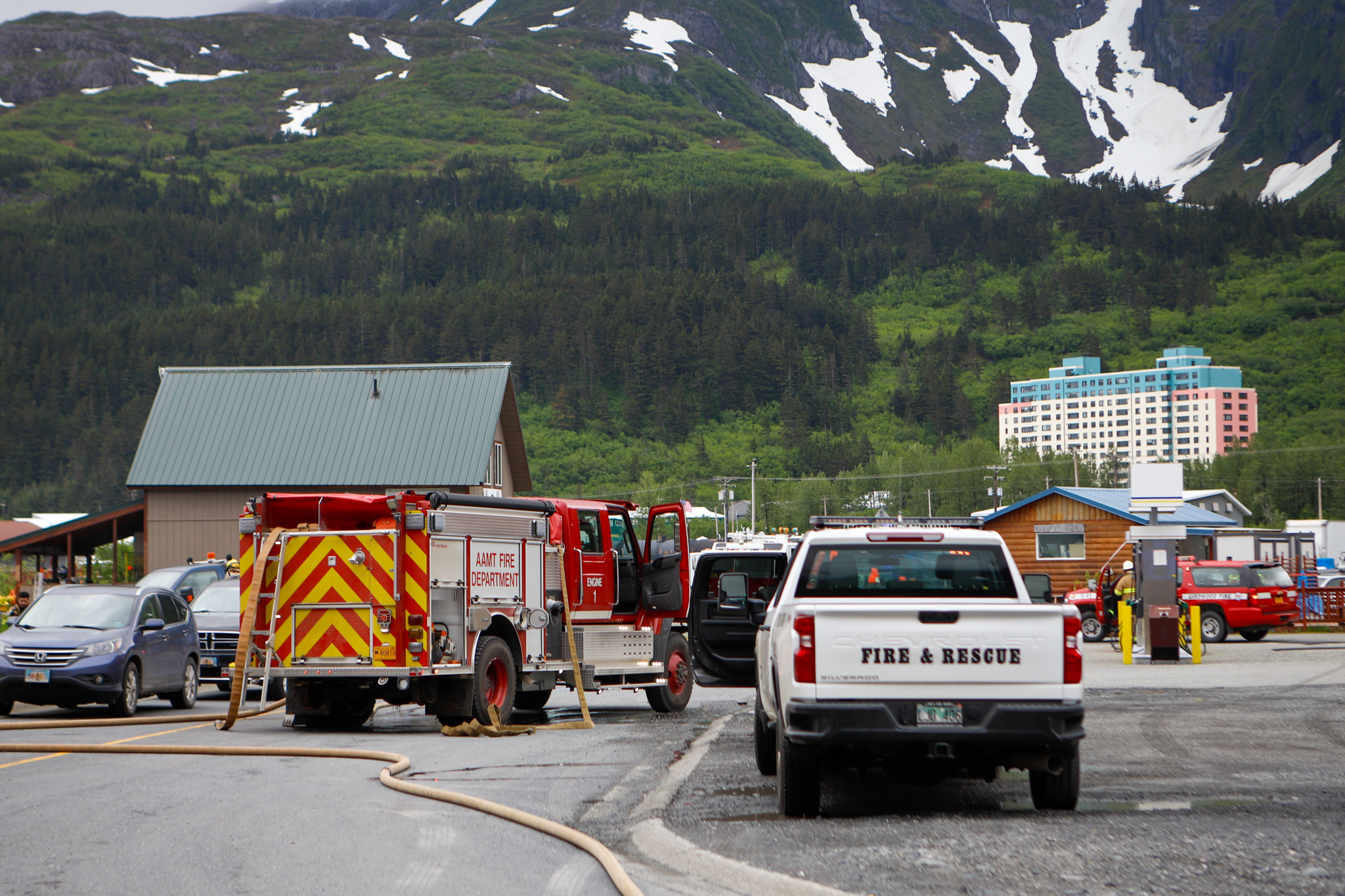 Fire trucks and hoses in front of a green, snow-capped mountain.