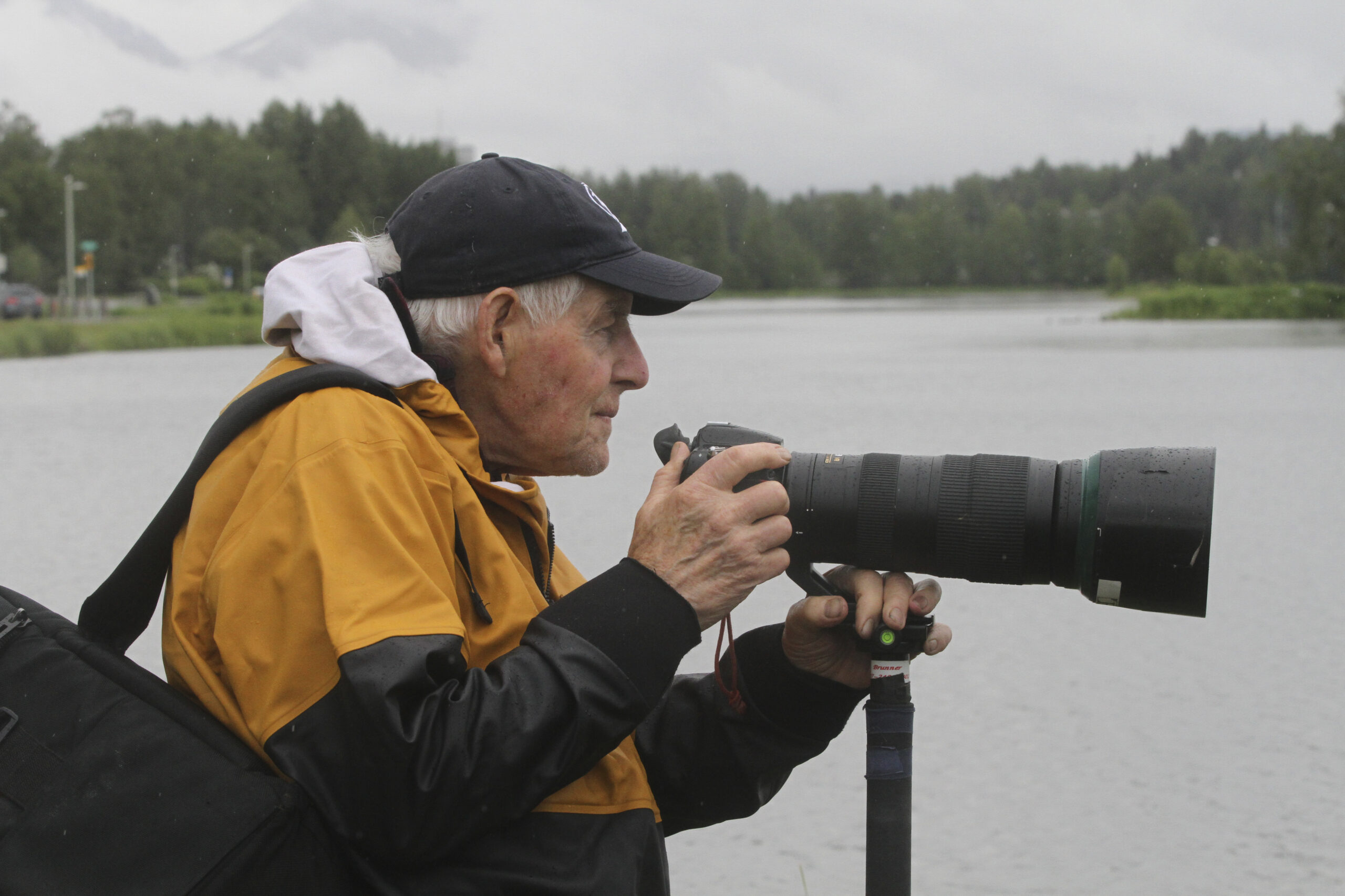 a man in a raincoat with a long lens camera