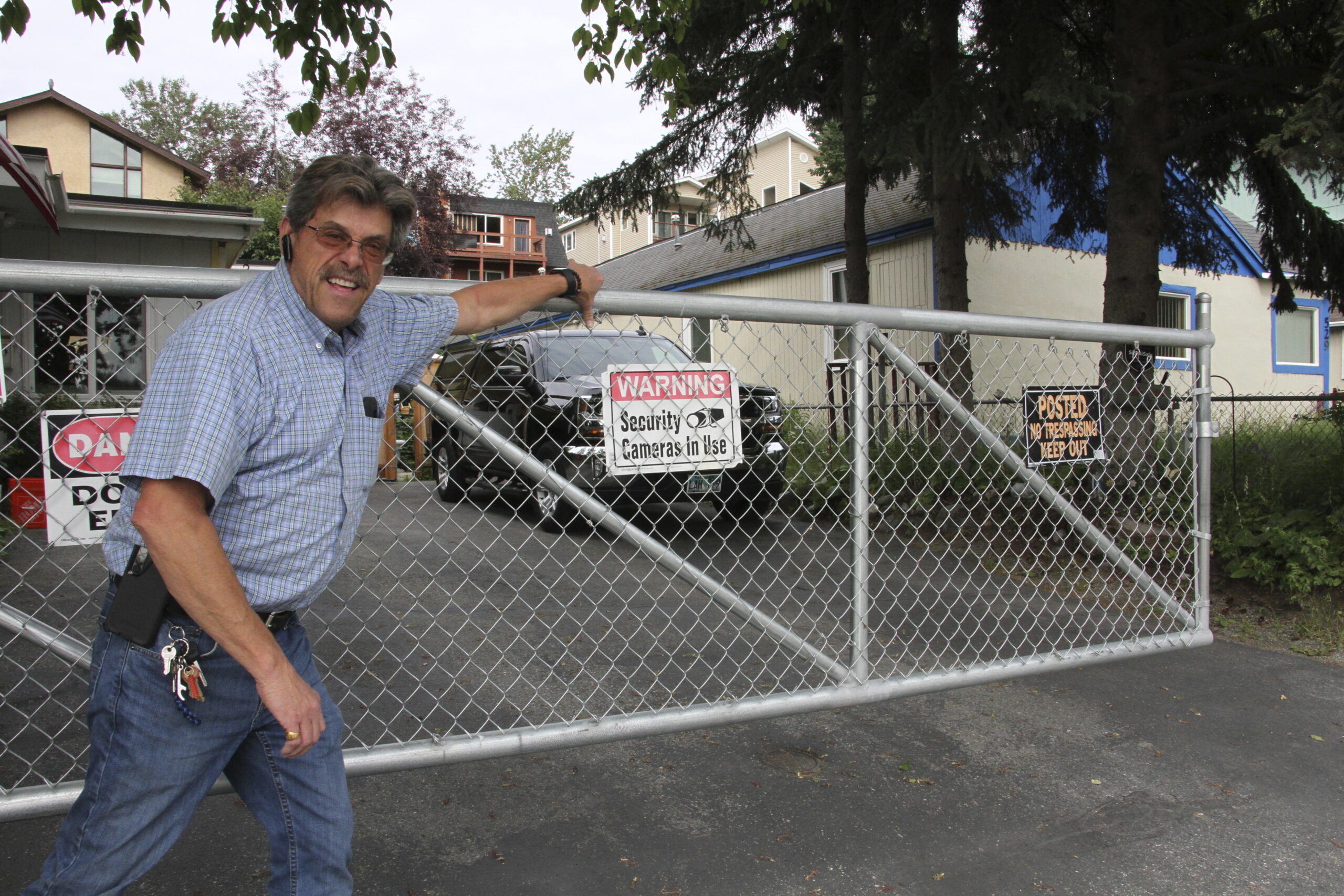 a man poses for a photo next to a gate with a sign that says warning, security cameras in use