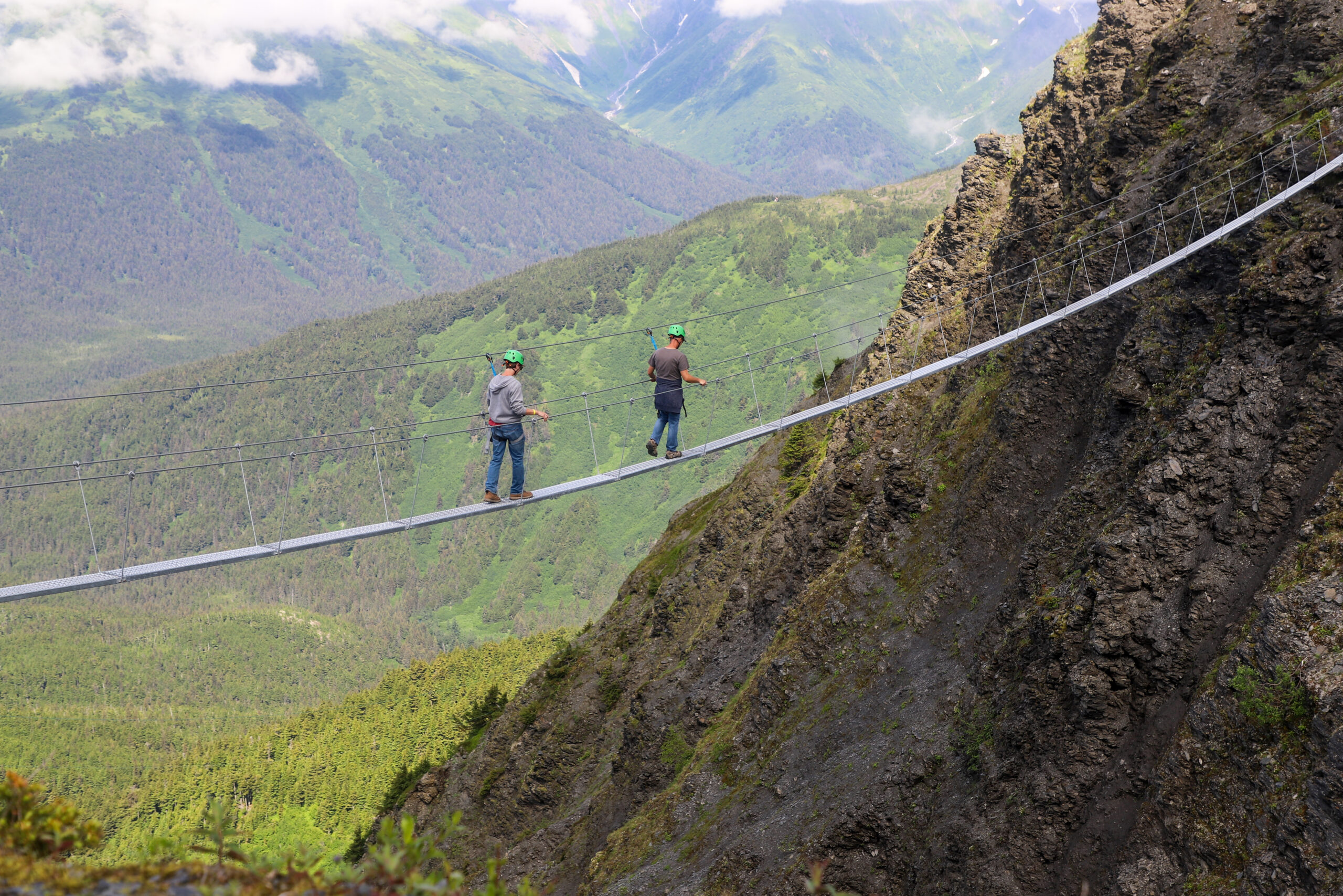 two people on a narrow bridge above a mountainside
