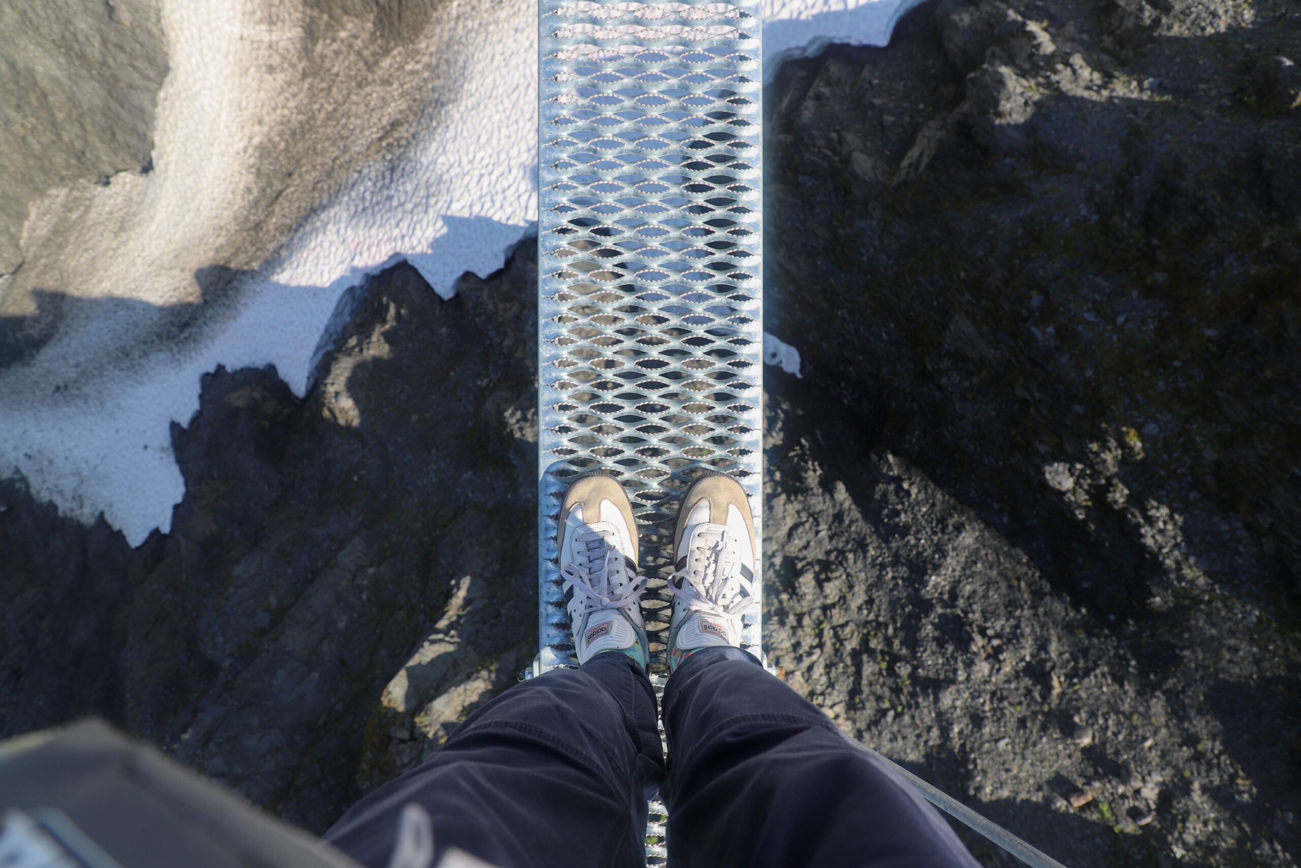 A person stands on a narrow bridge, looking down. It's only slightly wider than their two feet side by side.