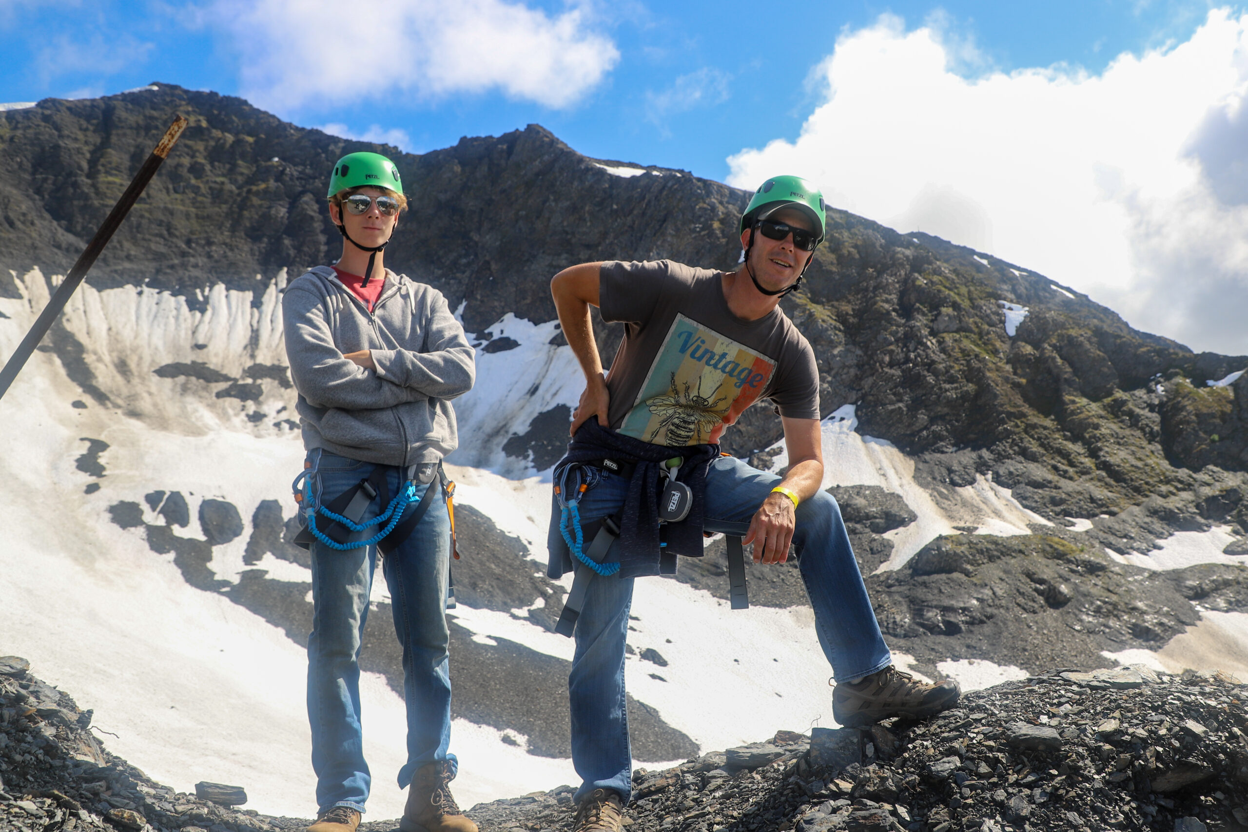Two people in climbing helmets and harnesses on top of a mountain.