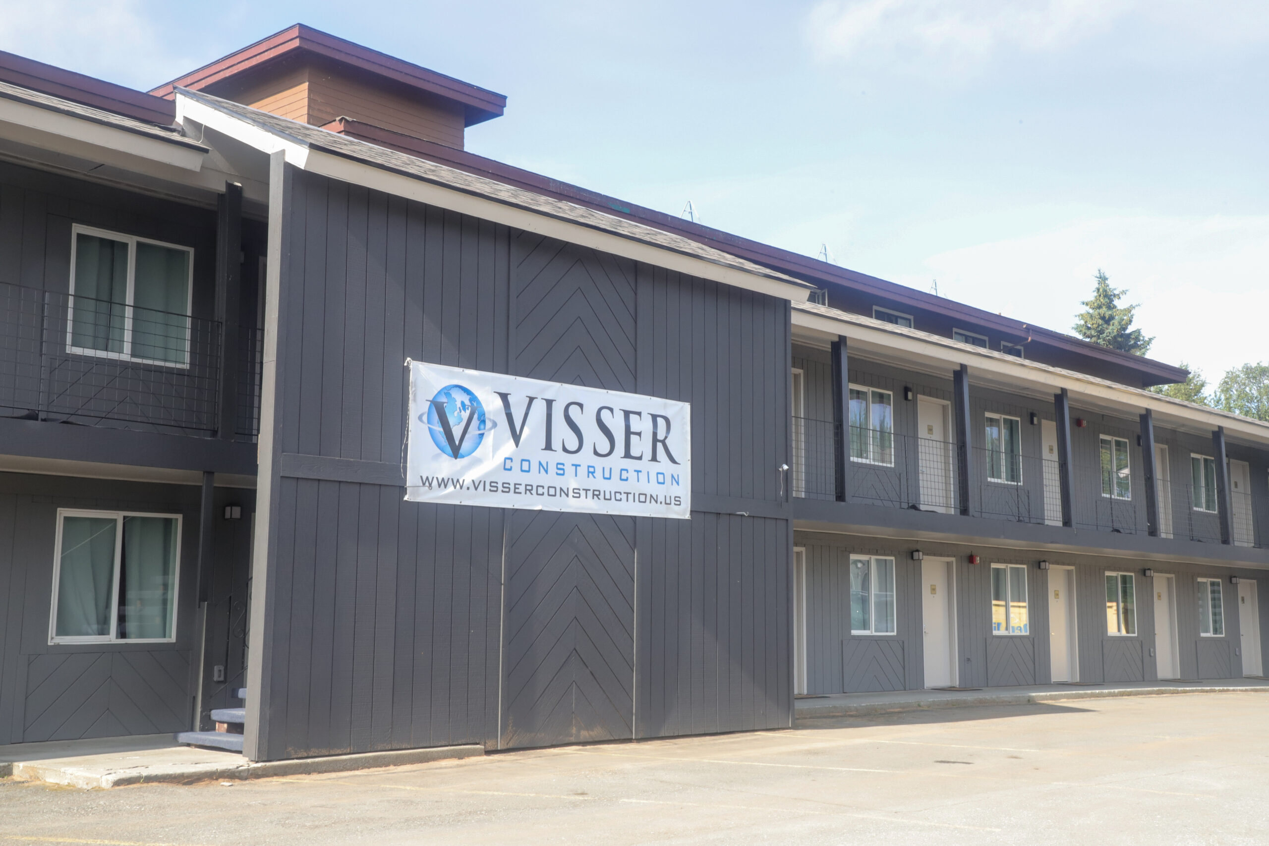 The exterior of a two story grey hotel building. A sign reading "Visser Construction" hangs from it.