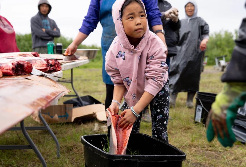 a girl holds a fileted salmon near a tote, outside