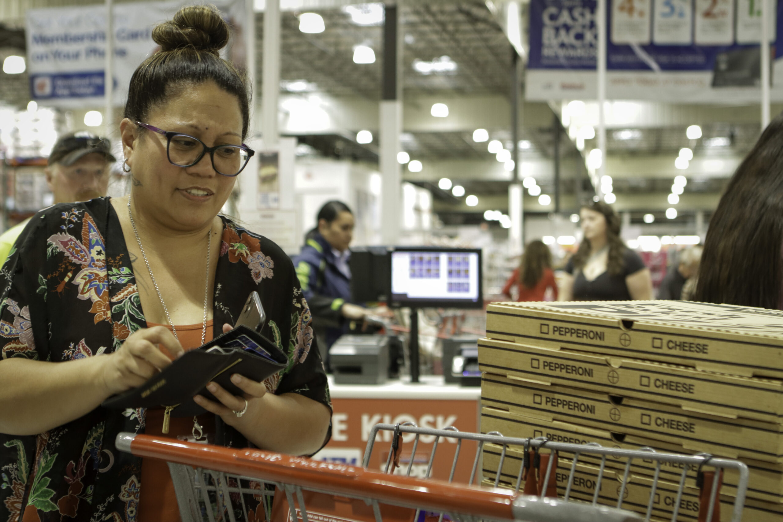 A woman is holding her wallet with a cart of pizzas at a Costco checkout line