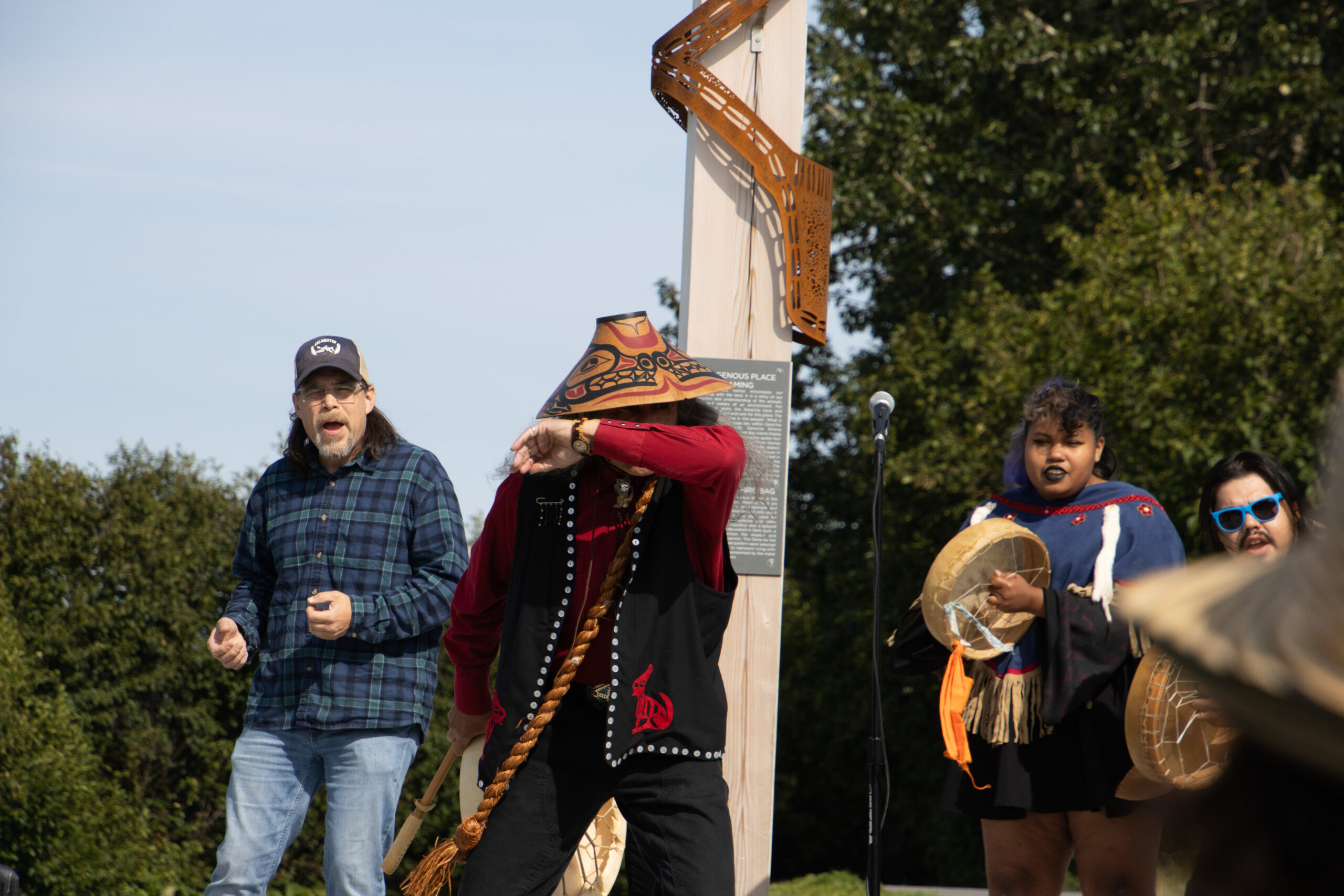 A Man dressed in Tsimshian regalia dances in front of a crowd as other tribe members perform at a signpost unveiling.