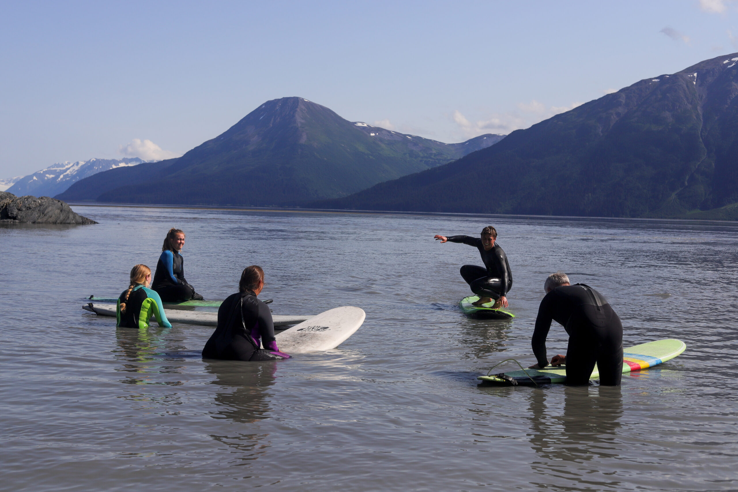 A group of people stand in shallow water with surfboards.